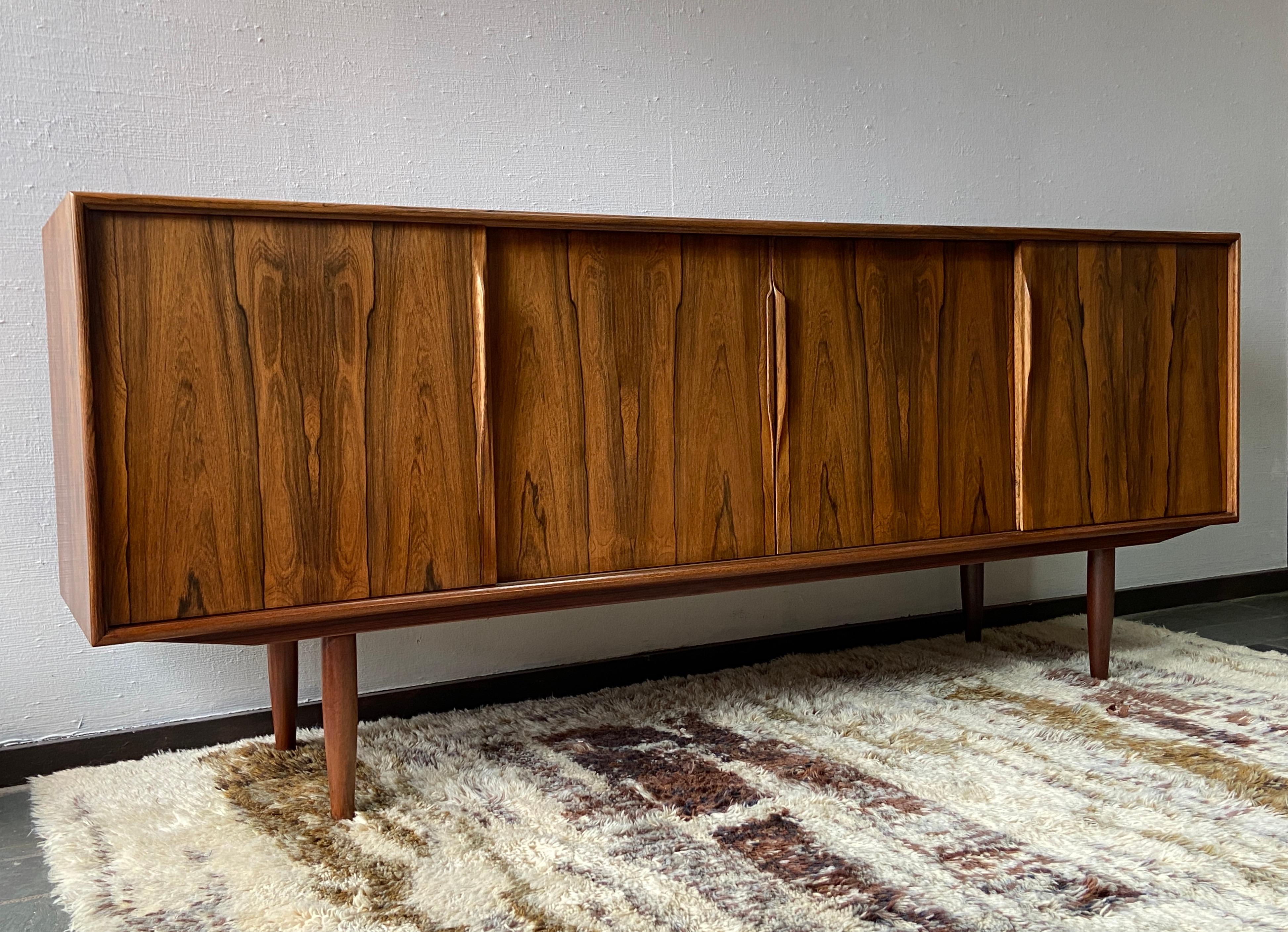 Splendida credenza - credenza in palissandro brasiliano di metà secolo disegnata da Gunni Omann e realizzata in Danimarca da AM Mobler - I. Christiansen.
Ha quattro porte scorrevoli con bellissime maniglie scultoree  che si aprono su un mobile con