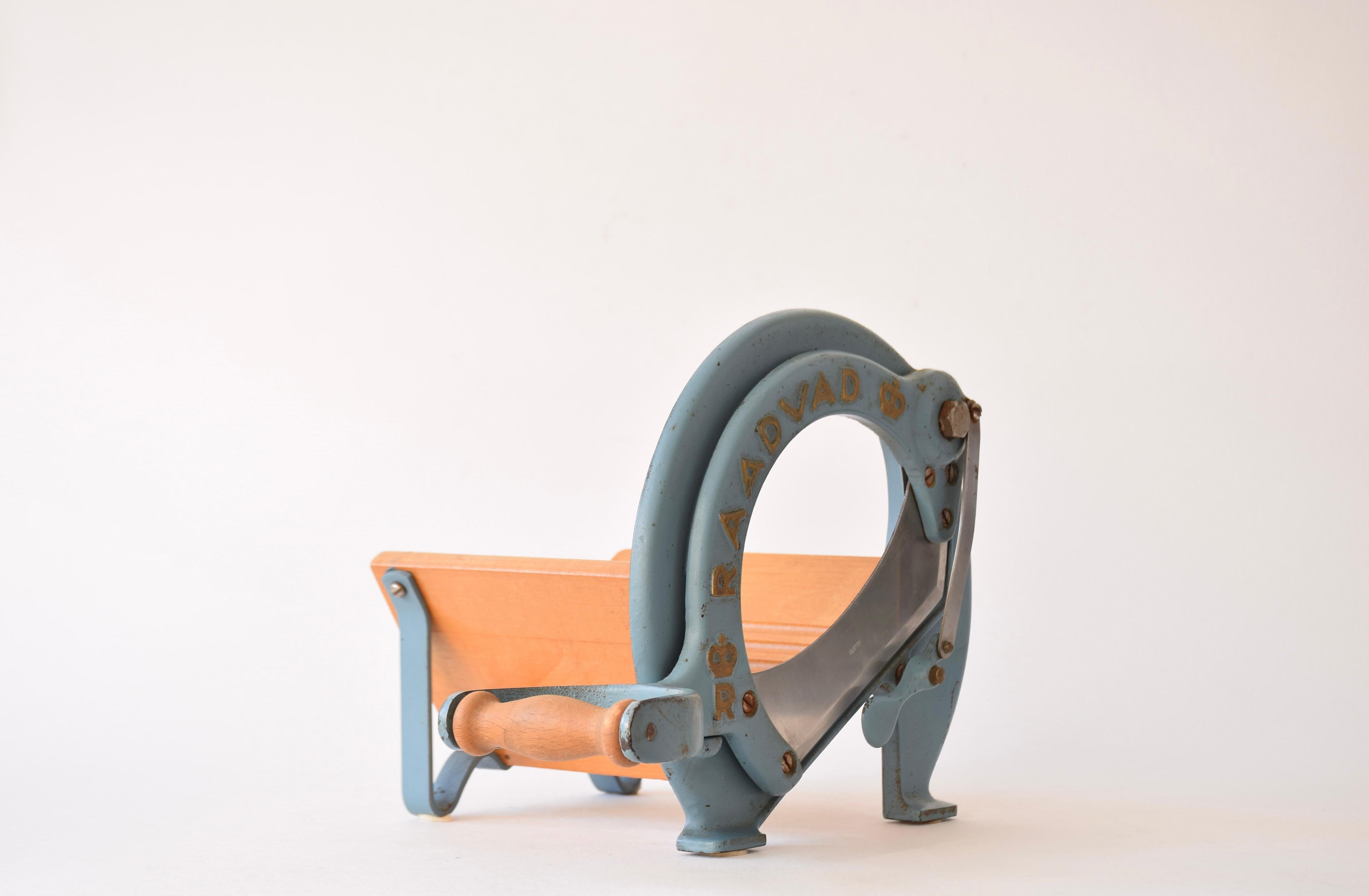 Questa iconica affettatrice danese è stata disegnata per Raadvad da Ove Larsen negli anni '30 e prodotta da Raadvad in Danimarca intorno agli anni '50. Viene fornito con la lacca originale blu e dorata. L'affettapane è perfettamente funzionale per