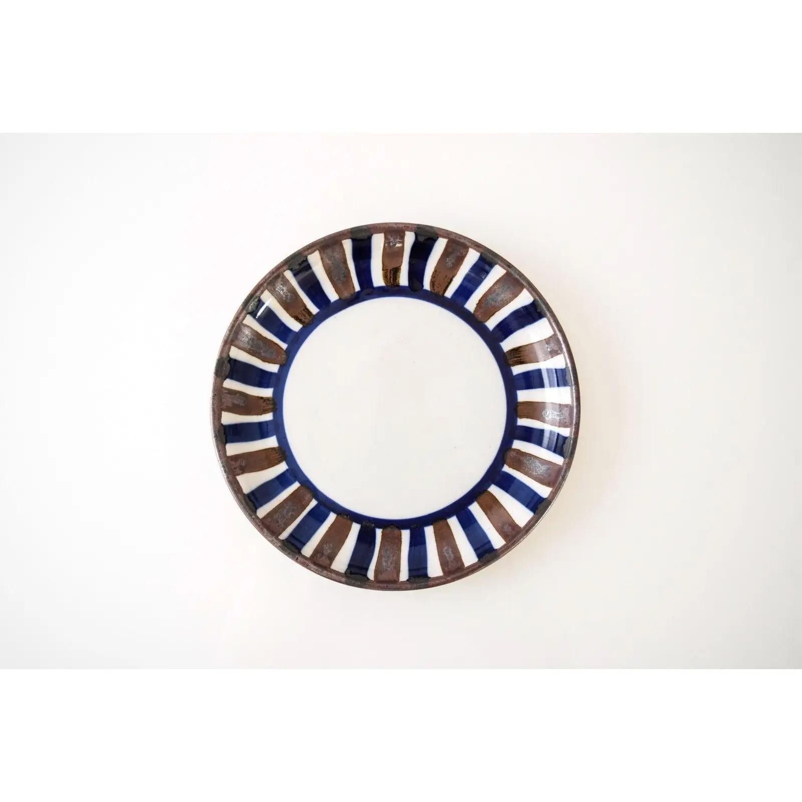 Diese kleine dekorative dänische Keramikschüssel aus der Mitte des Jahrhunderts, um 1960, hat ein schönes flaches Profil. Das schlichte, modernistische Design zeichnet sich durch organische, handgemalte blaue und braune Streifen aus.

Abmessungen: