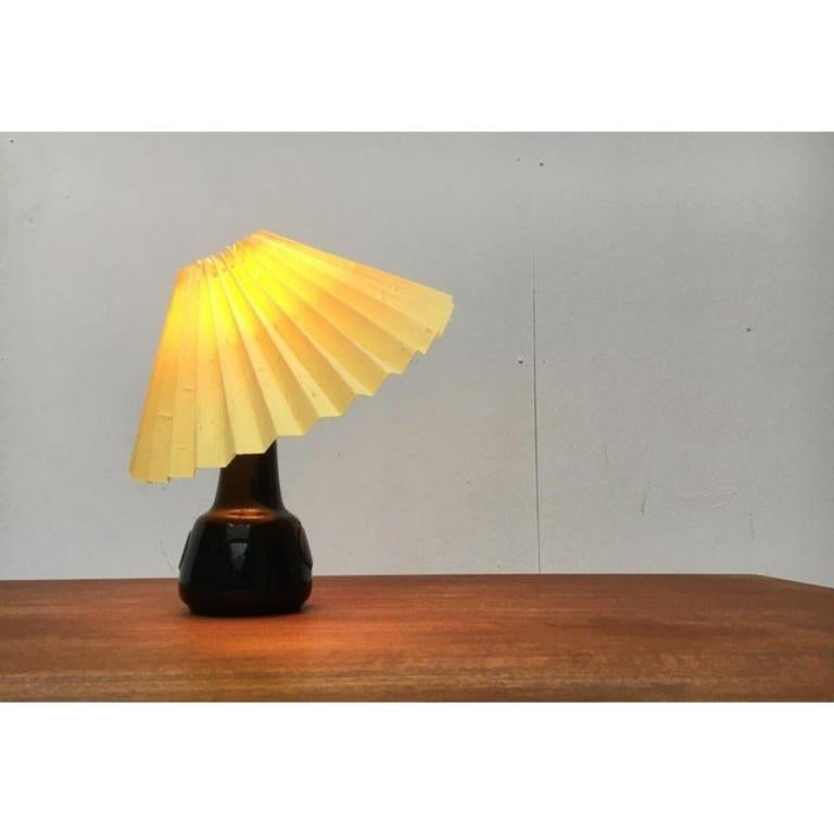 mall ceramic table lamp from the Danish manufacturer Søholm from the 60's.
 
The conical pleated shade sits with a clamp directly on the lamp. This kind of mounting allows a manual adjustment of the shade. The glazed ceramic base shows a typical