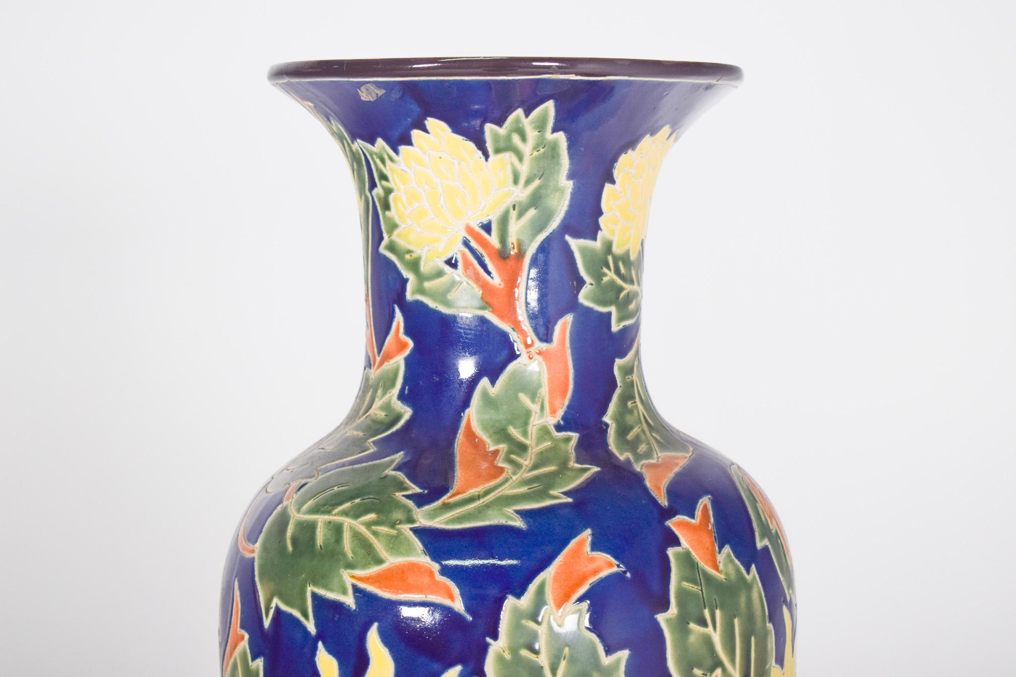 Vaso in ceramica dipinta. Decorazione policroma con sfondo blu intenso, che funge da base per un dettagliato motivo floreale, composto da foglie verdi, fiori gialli e dettagli rossi. Il design dei fiori assomiglia a girasoli stilizzati, con facce
