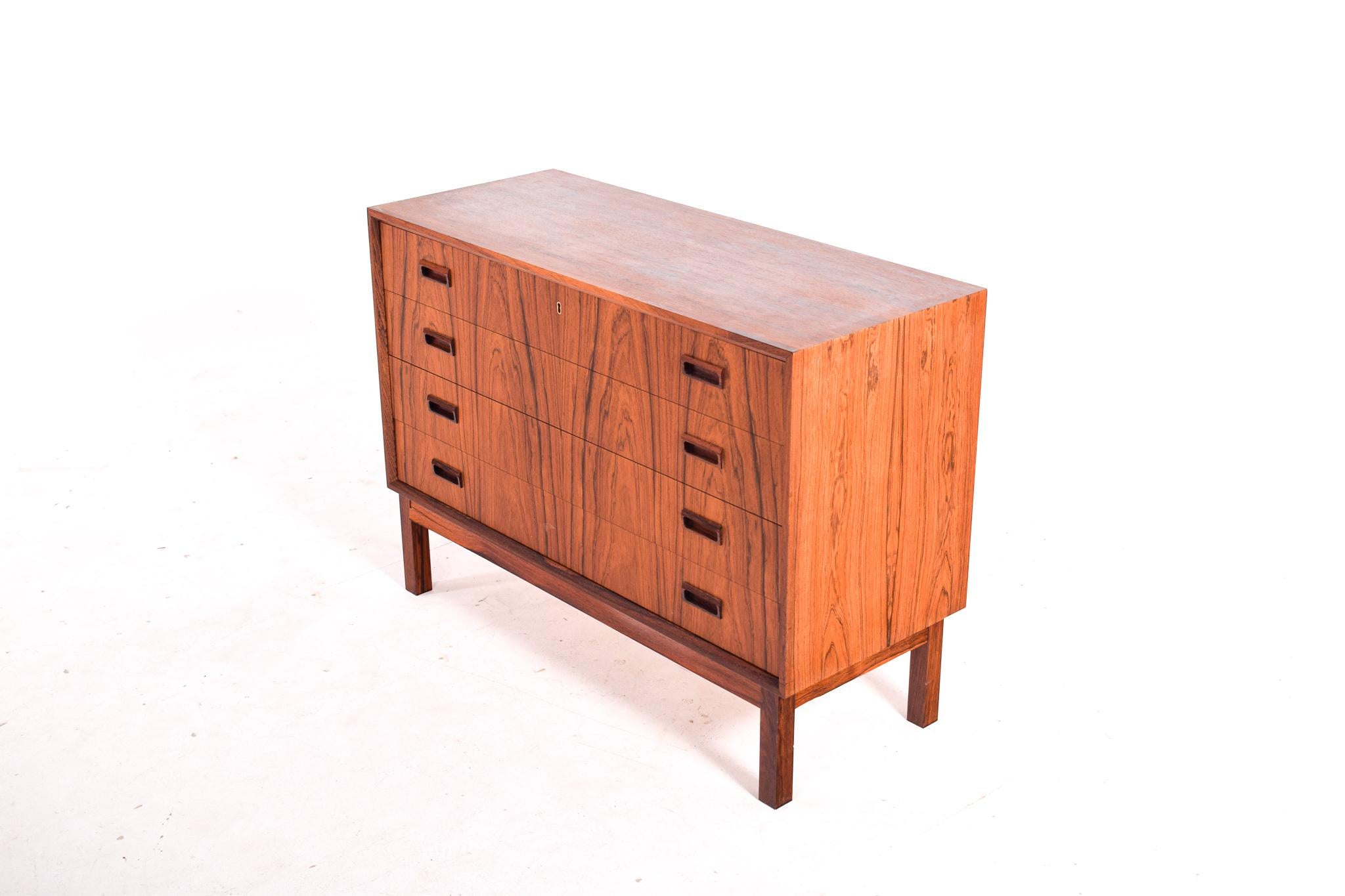 A Mid-Century Modern chest of drawers standing on legs with inset handles. It has four drawers that all run smoothly, one of the drawers has a lock. The chest has been refinishing and is in excellent condition.