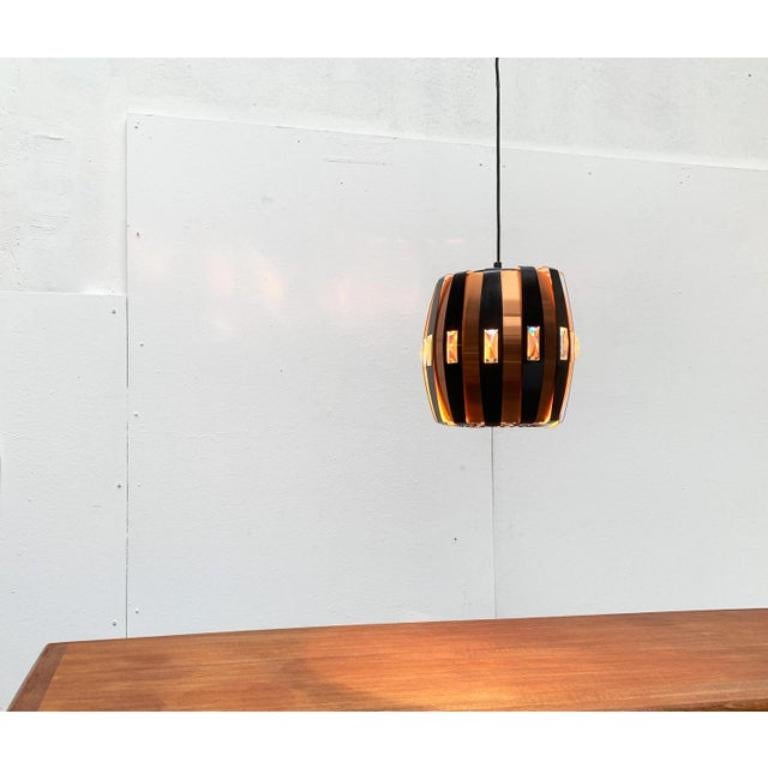 Danish mid-century pendulum by Coronell Elektro based on a design by Werner Schou from the 70s.

An imposing and solemn design. The body of the lamp consists of radially arranged metal strips in copper and black. The slats are arranged in different
