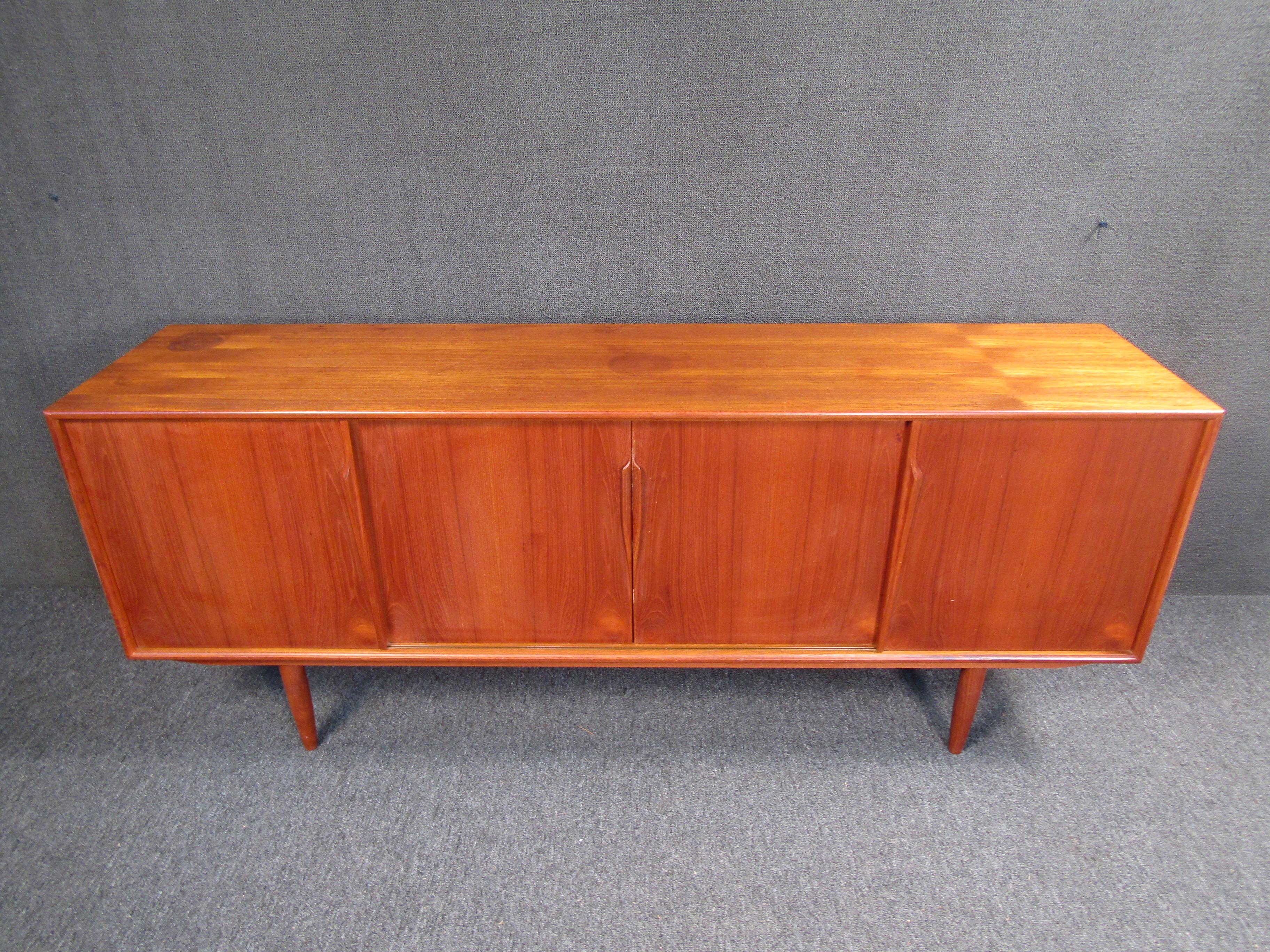 Take advantage of a rare opportunity to bring home genuine vintage luxury Danish design with this incomparable credenza designed by Axel Christiansen Odder and built by the artisanal craftsmen of Aco Møbler. Four sliding teak doors open to reveal