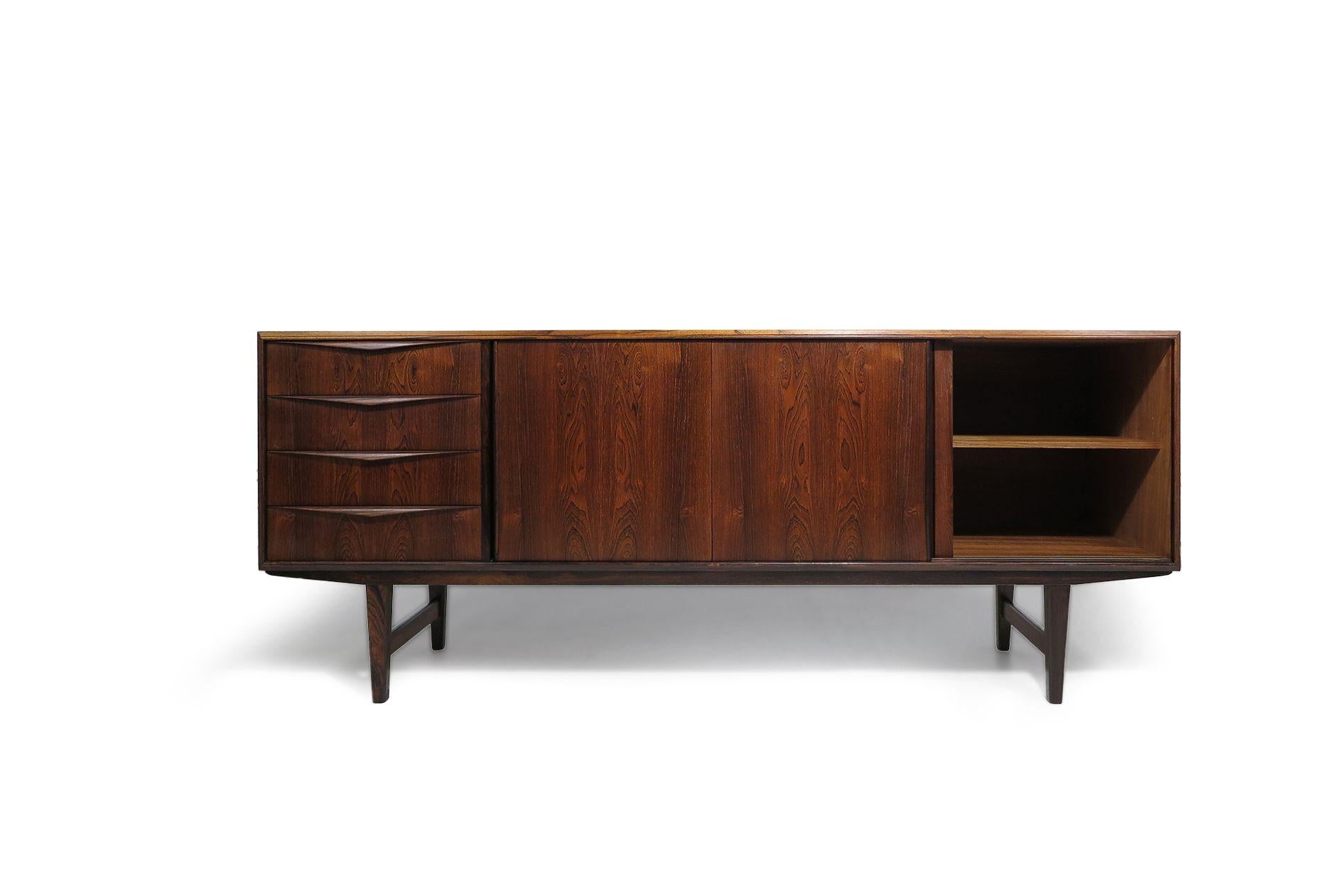 Danish rosewood credenza handcrafted from stunning Brazilian rosewood, featuring a mitered cabinet frame, three sliding doors, and a series of four drawers with book-matched grain and sculpted pulls. The sliding doors open to reveal an interior of