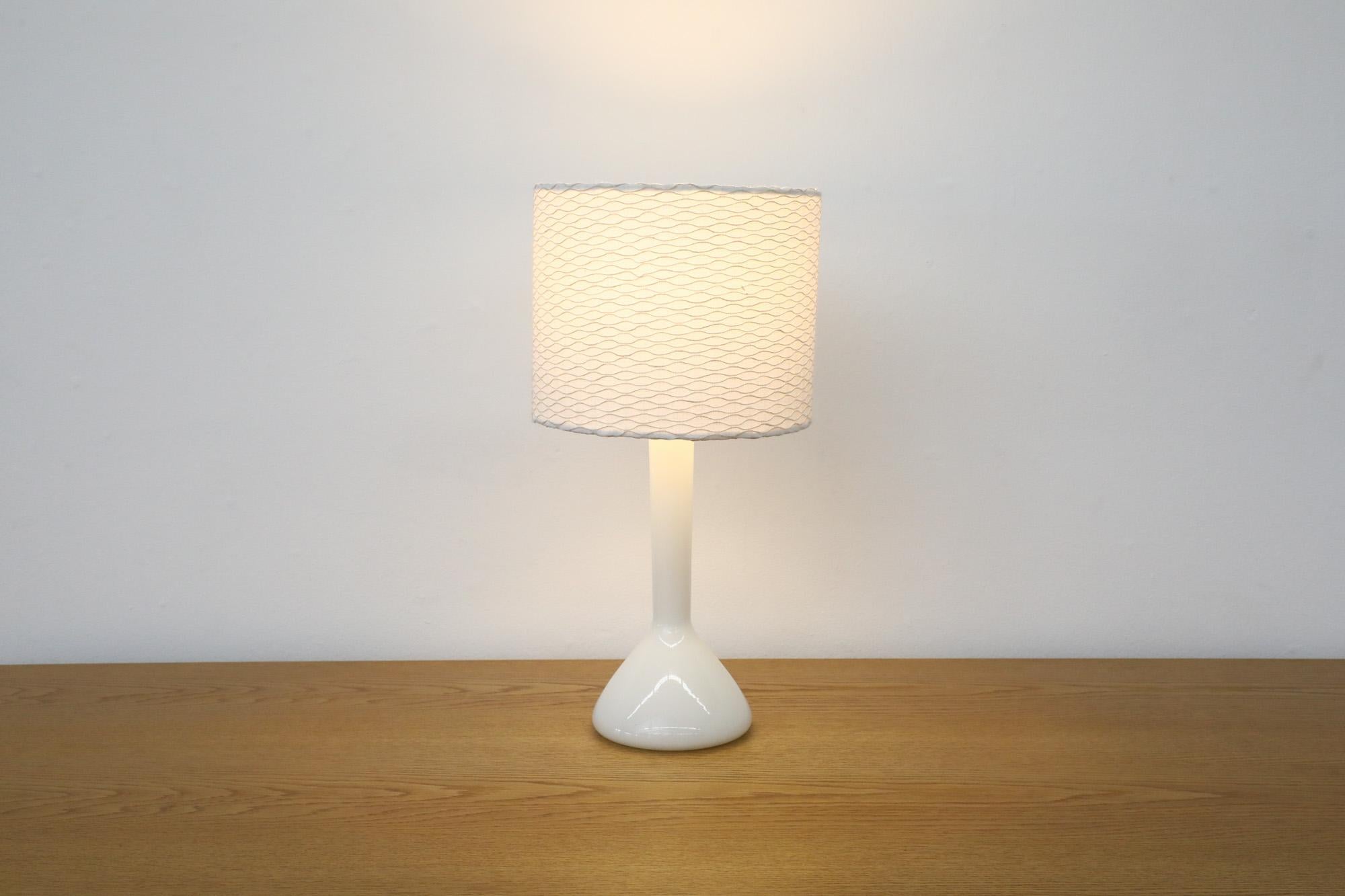 Lampada da tavolo in vetro di Holmegaard, design danese di metà secolo. La lampada è in vetro bianco latte con paralume in tessuto testurizzato bianco. Utilizza una lampadina standard E26/E27 a base media. In condizioni originali, con un'usura e un