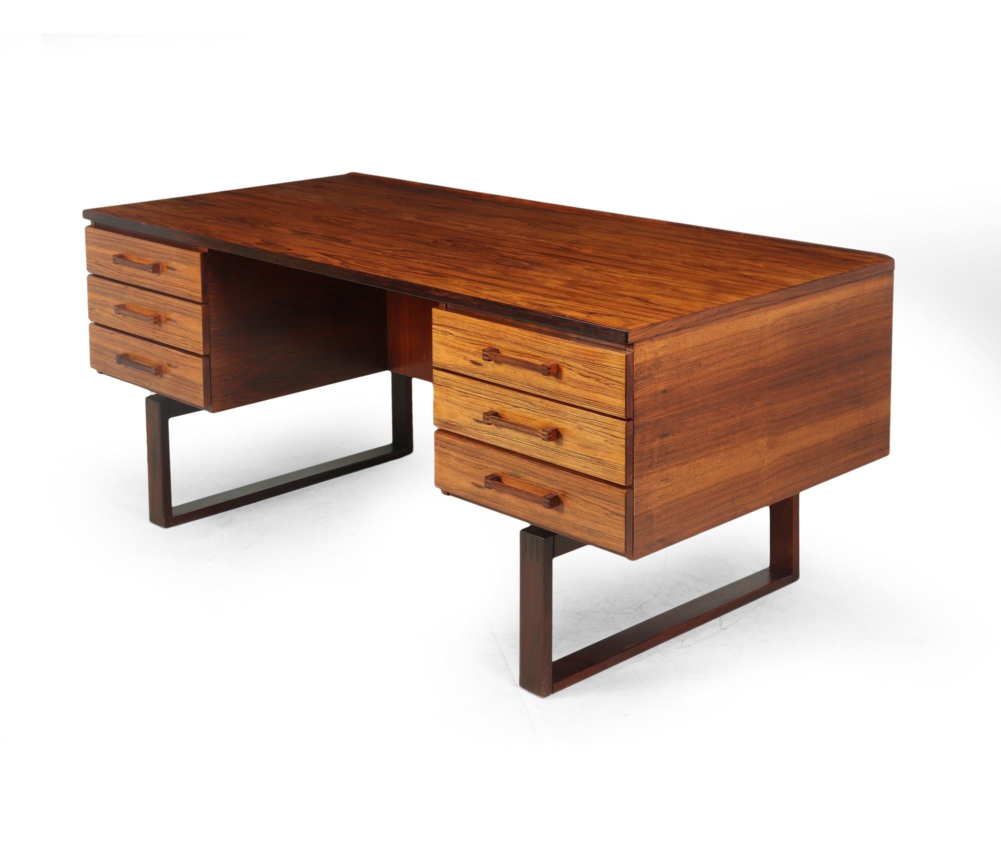 A classic six drawer mid century Danish desk in rosewood by Henning Jensen and Torbin Valeur featuring finger jointed handles and sled legs, raised lip to the back with bookshelf below, the desk has be restored where necessary and polished by hand