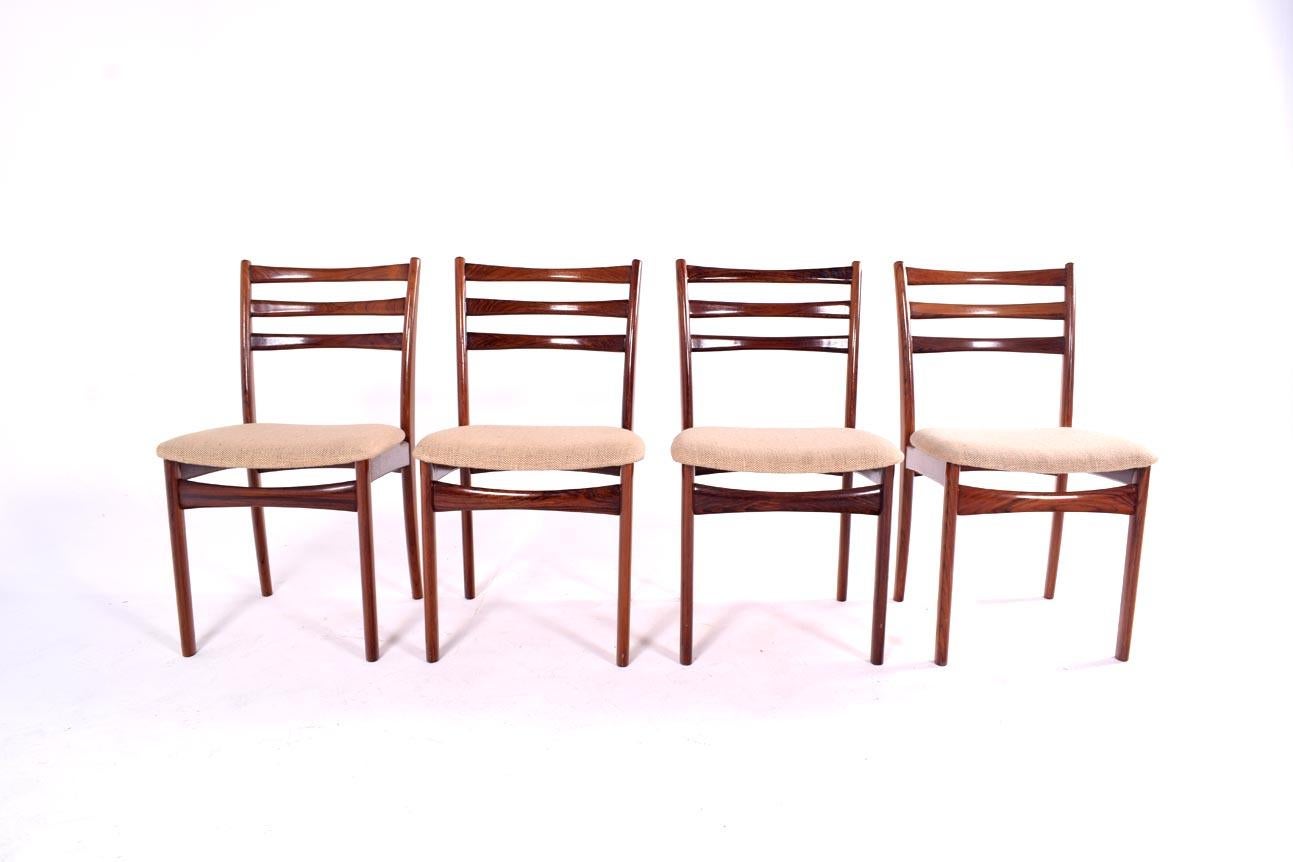 This sleek set of four dining chairs features stunning rosewood frames with ladder backrests, combining a rich, dark wood finish with modern design elements. The padded seats, upholstered in a neutral fabric, ensure maximum comfort while dining, and