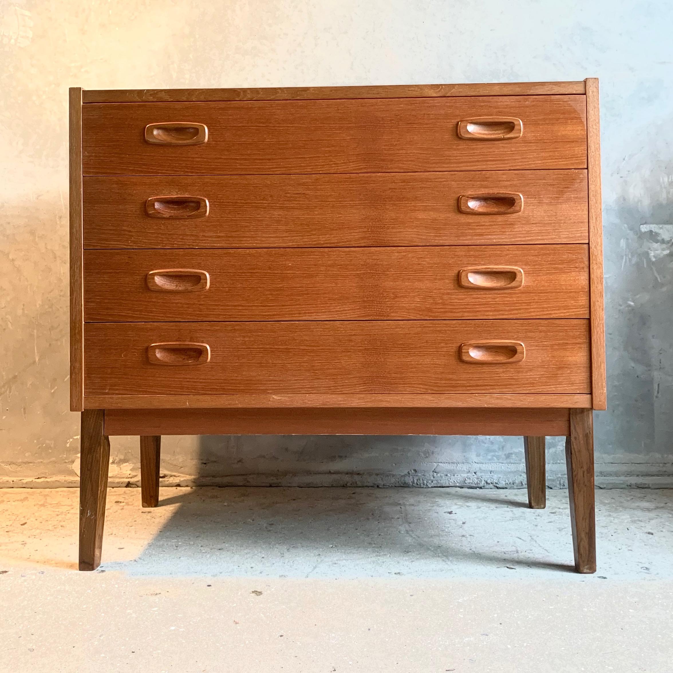 This midcentury teak dresser was produced in Denmark by PS Furniture Randers in the 1960s. It is in good vintage condition and features four drawers, tapered legs, and curved handles. The model is B 330.