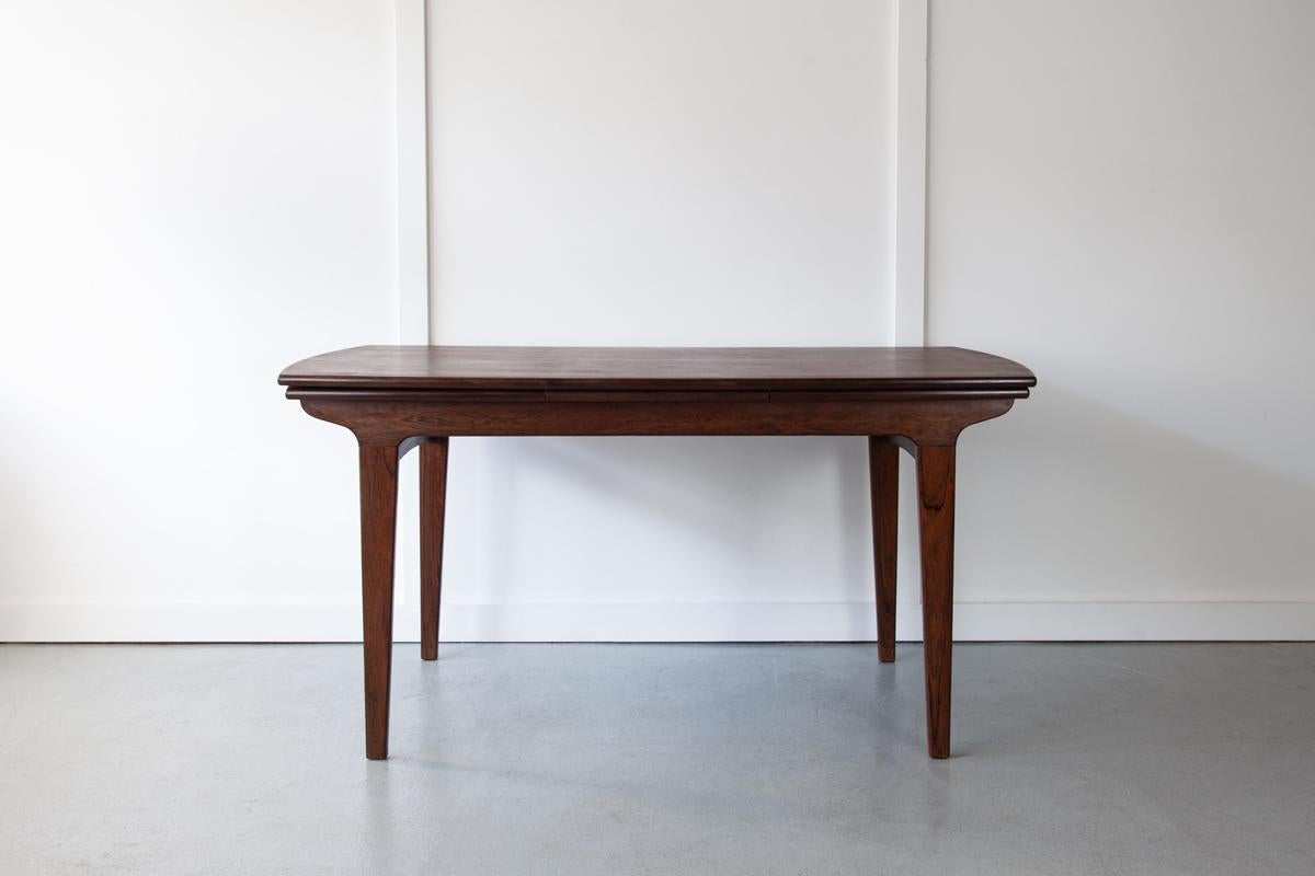 A beautiful Danish 'surfboard' dining table in rosewood with two extending leaves which slide out either end, one by one, from beneath the table top to allow for large gatherings of 8-10 people. The table top is beautifully grained and finished with