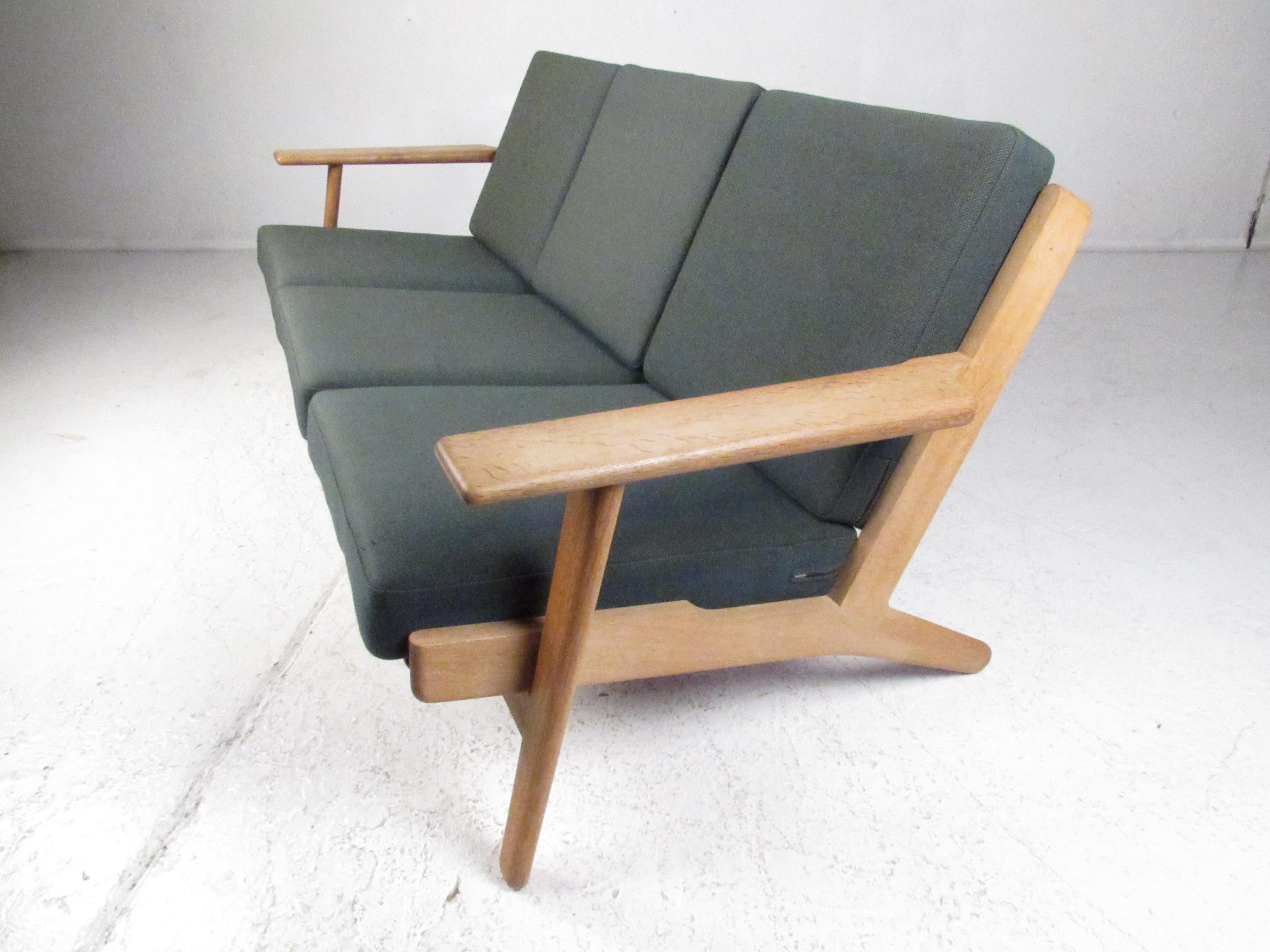 Dieses schöne moderne Dreisitzer-Sofa im Vintage-Stil verfügt über einen massiven Rahmen aus blonder Eiche mit breiten, geschwungenen Armlehnen und gespreizten Beinen. Ein bequemes Sofa mit sechs abnehmbaren Kissen, bezogen mit einem grünen
