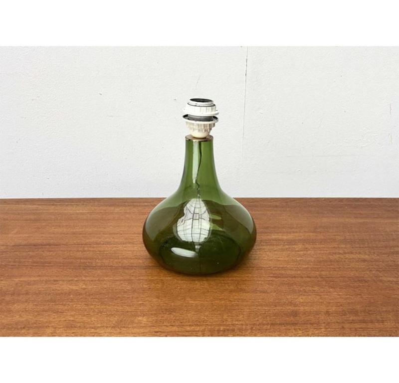 Lámpara de sobremesa con base de cristal verde de los años 60. Probablemente del fabricante danés Holmegaard.

Un diseño tradicional. Esta lámpara de sobremesa impresiona por su base ornamental de cristal coloreado. El cristal transparente es verde.