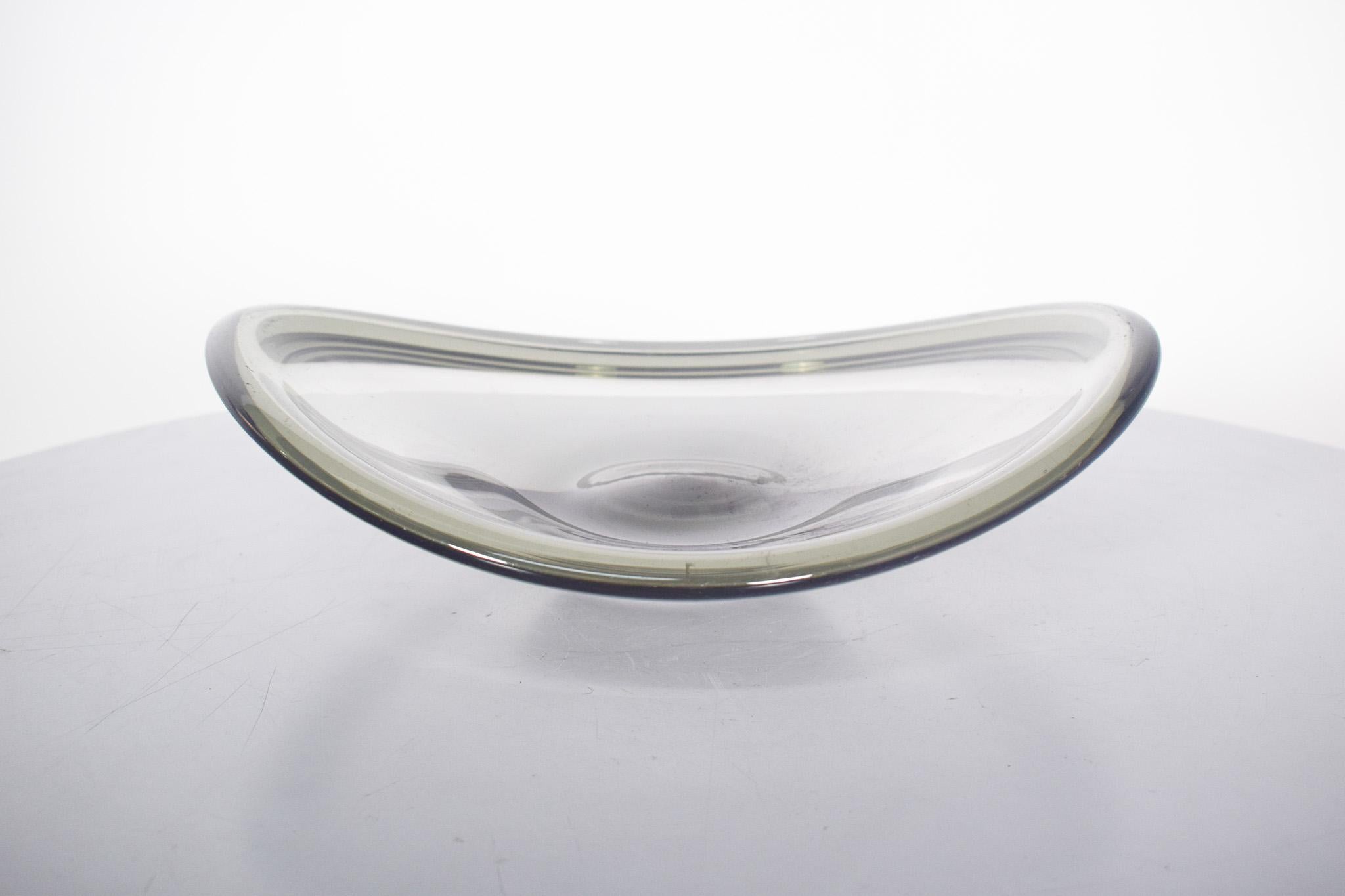 Ciotola in vetro grigio. Vetro soffiato con forma allungata e bordi alti e curvi. Il vetro è spesso e trasparente, con una tonalità grigiastra, quasi 