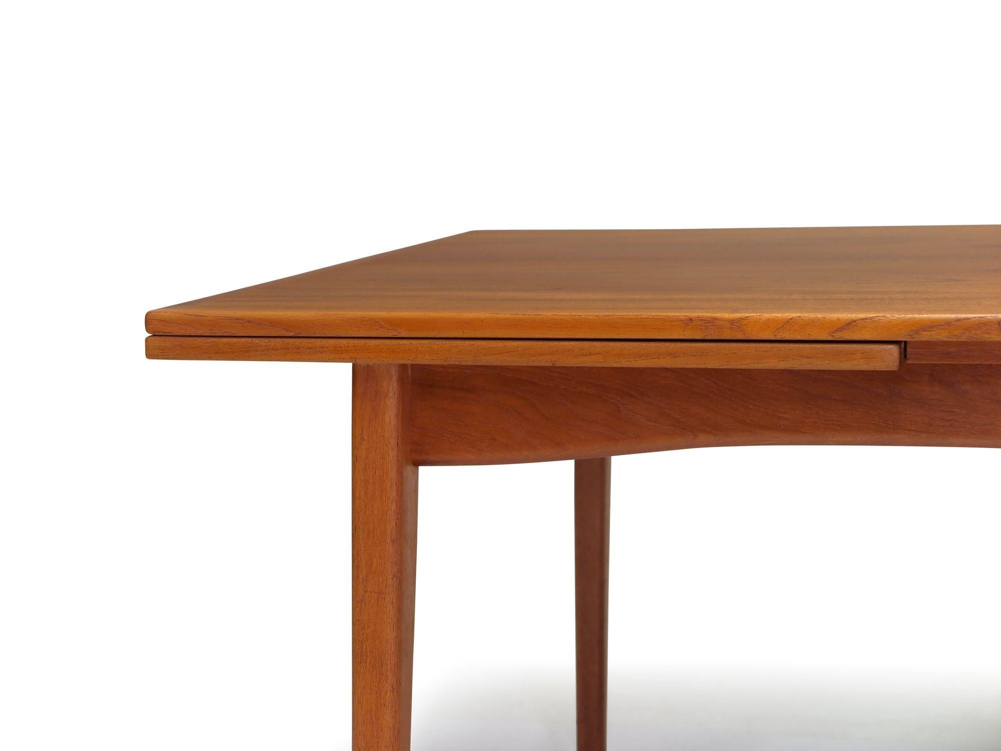 Rectangular teak dining table by H. Sigh & Son, crafted in 1965 in Denmark. This table showcases book-matched grain, solid wood edge banding, and two draw-leaves on either end. Raised on tapered legs, it comfortably seats 6 guests when closed and