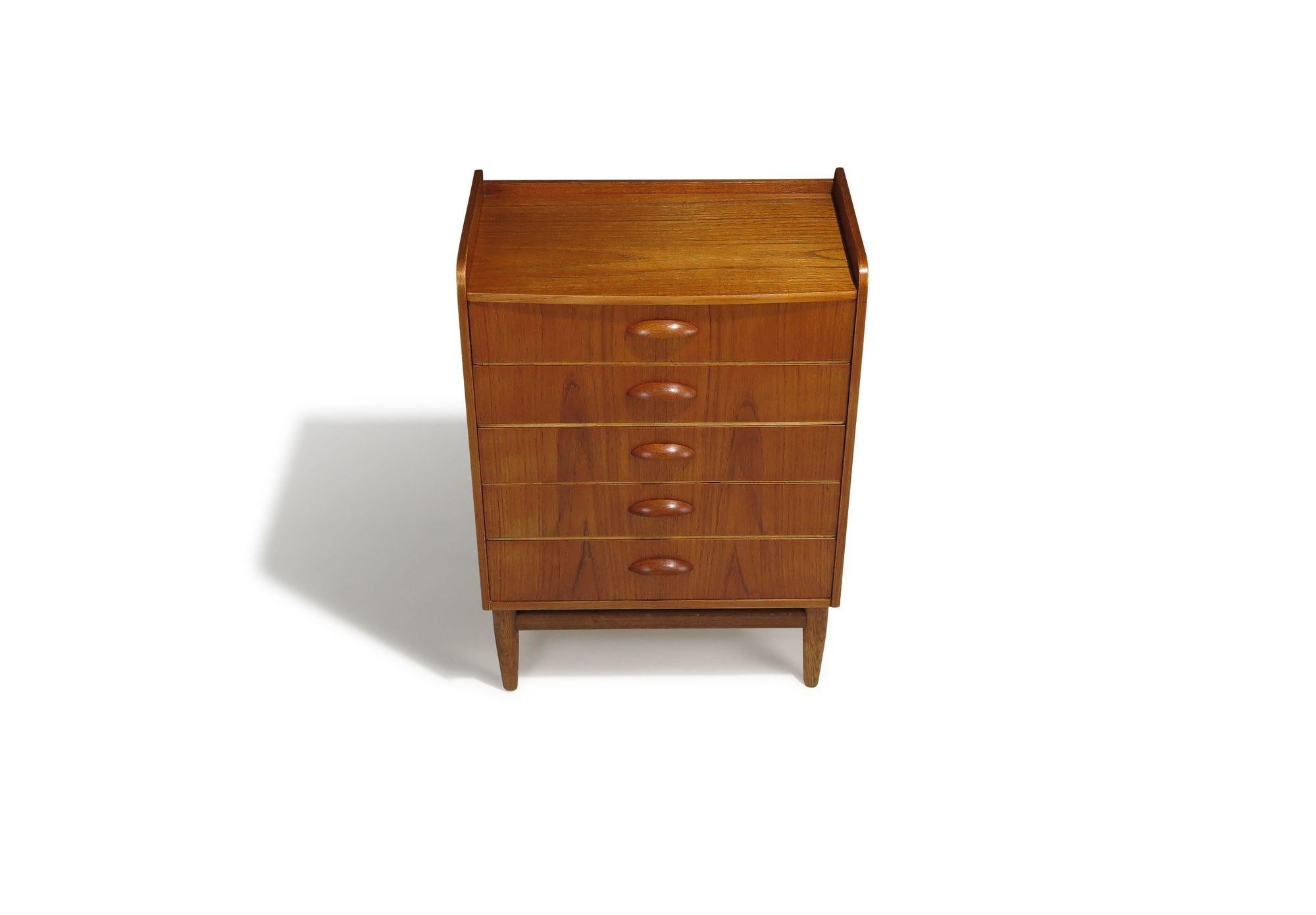 Finely handcrafted in Denmark in 1960, this elegant small chest is designed by Kai Kristiansen and built from richly grained old-growth teak. It features a subtly bowed front with five drawers, each adorned with half-circle carved pulls and