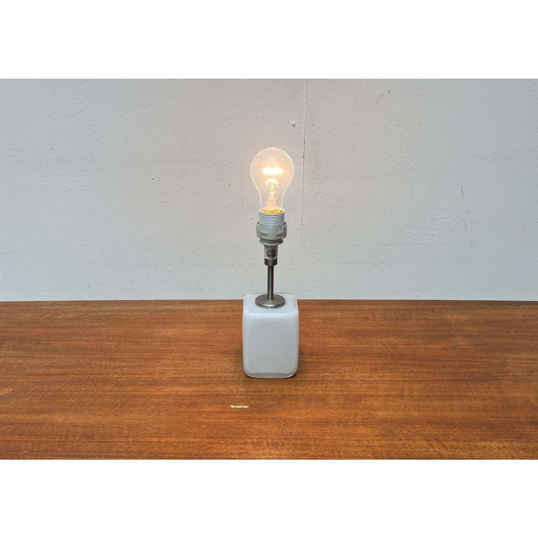 Una sencilla lámpara de sobremesa con base de cristal cúbico del fabricante danés Holmegaard, diseñada por Per Lütken.

Un diseño minimalista. Esta lámpara de sobremesa impresiona con su sencilla base de cristal opalino. Las pantallas a juego están