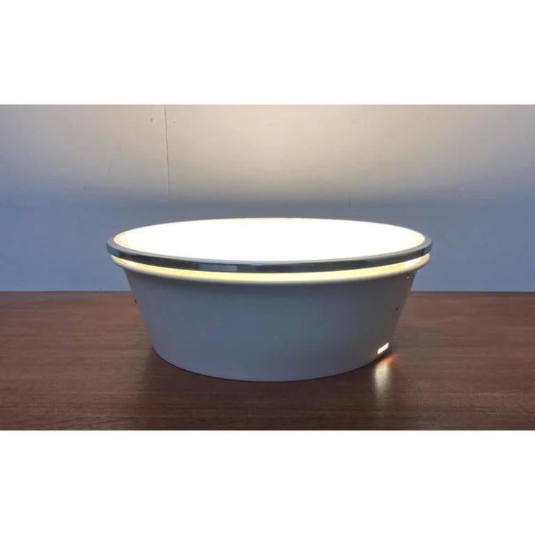 Grande plafoniera da incasso di Arne Poulsen basata su un disegno di Arne Jacobsen degli anni '50. Qui nella versione con bordo cromato.

plafoniera minimalista in metallo e vetro. La lampada è composta da un riflettore bianco e da un disco
