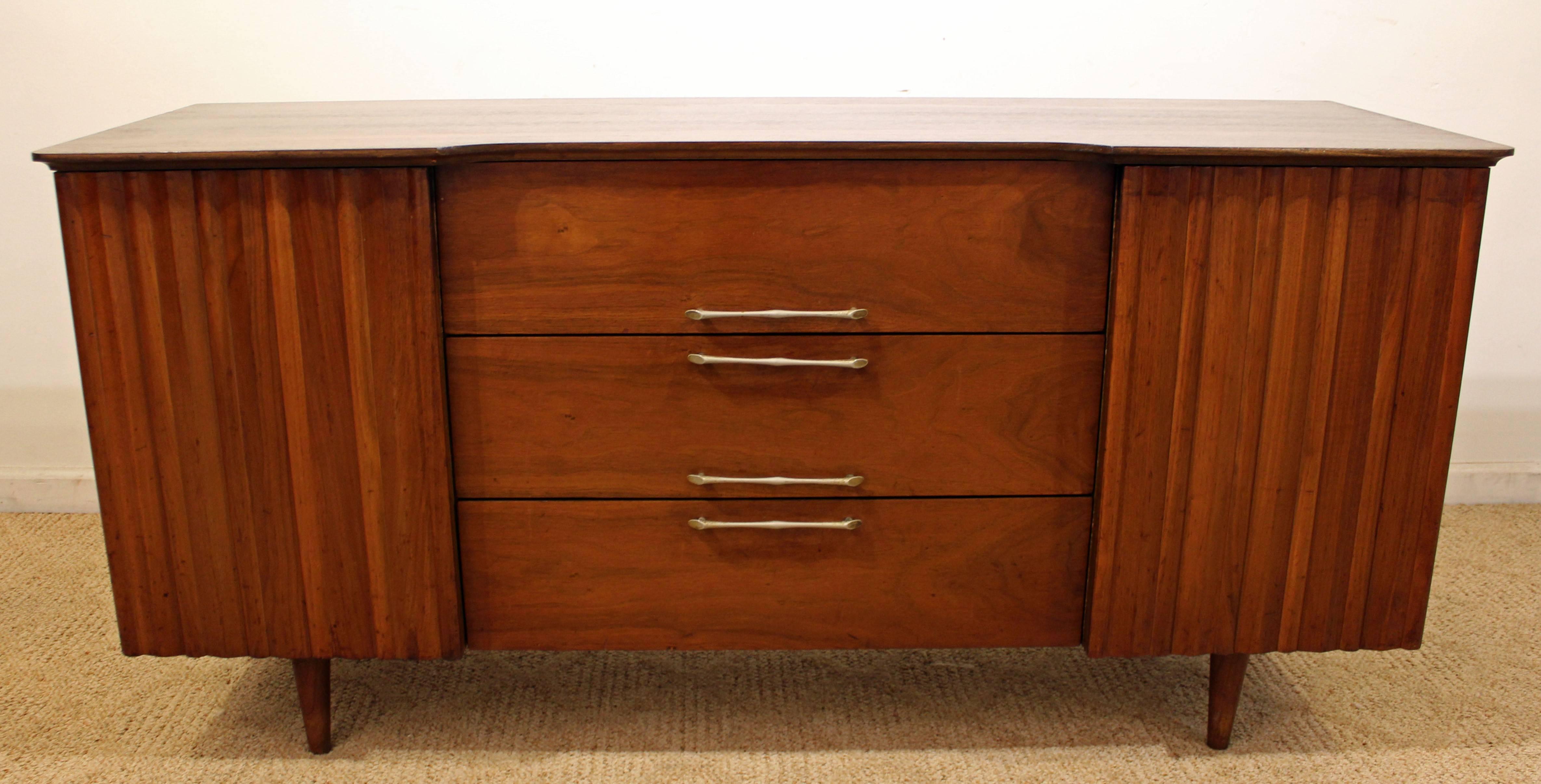 Offered is a mid-century credenza made of walnut, featuring two sculpted doors with shelving inside and three drawers. 