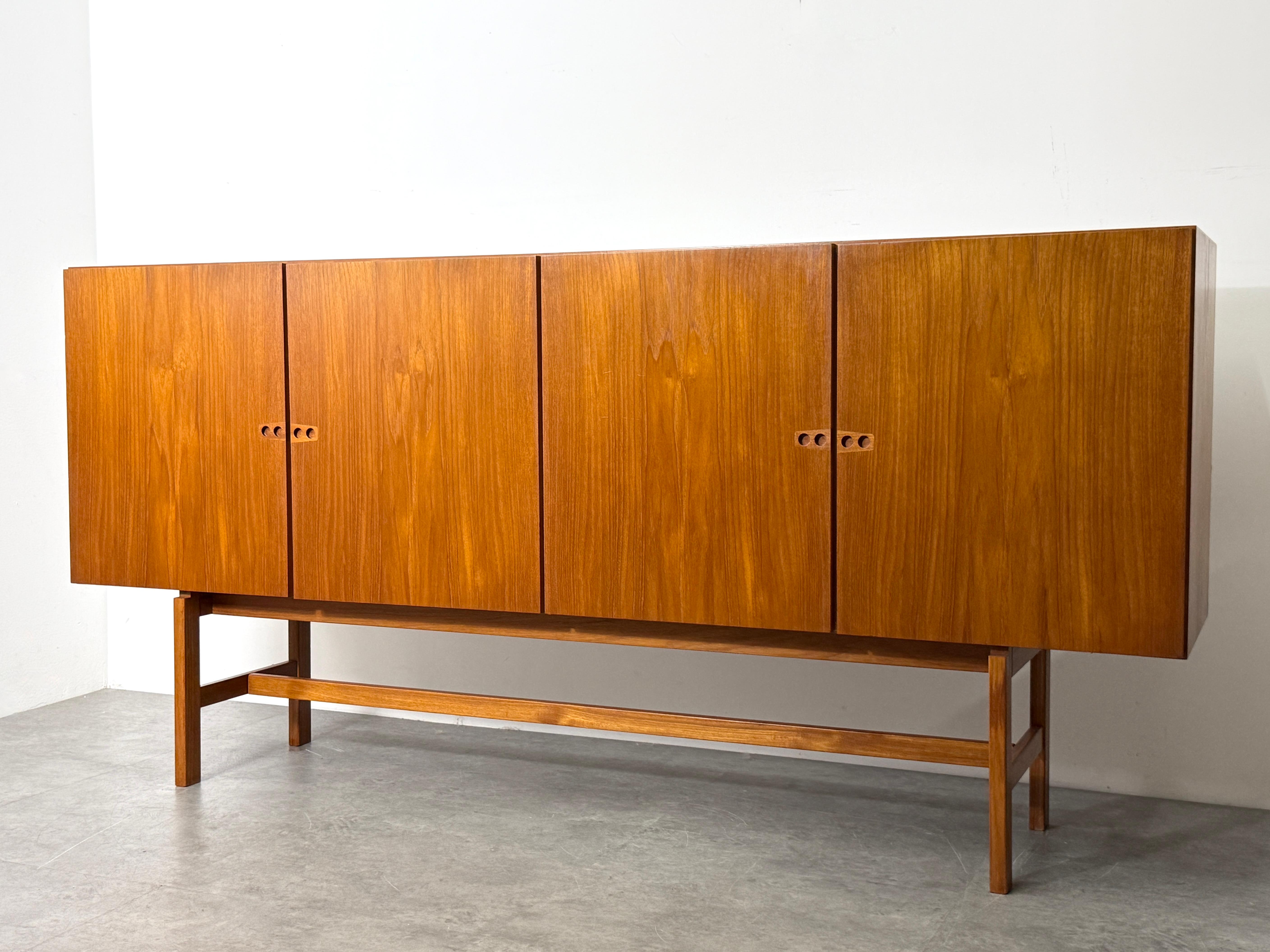 Monumental sideboard or credenza by Arne Vodder circa 1960

Tall and stately four door cabinet in rich teak with unique recessed finger pulls 
Elevated open frame base in solid teak
 
Left side features two storage drawers with upper fixed glass