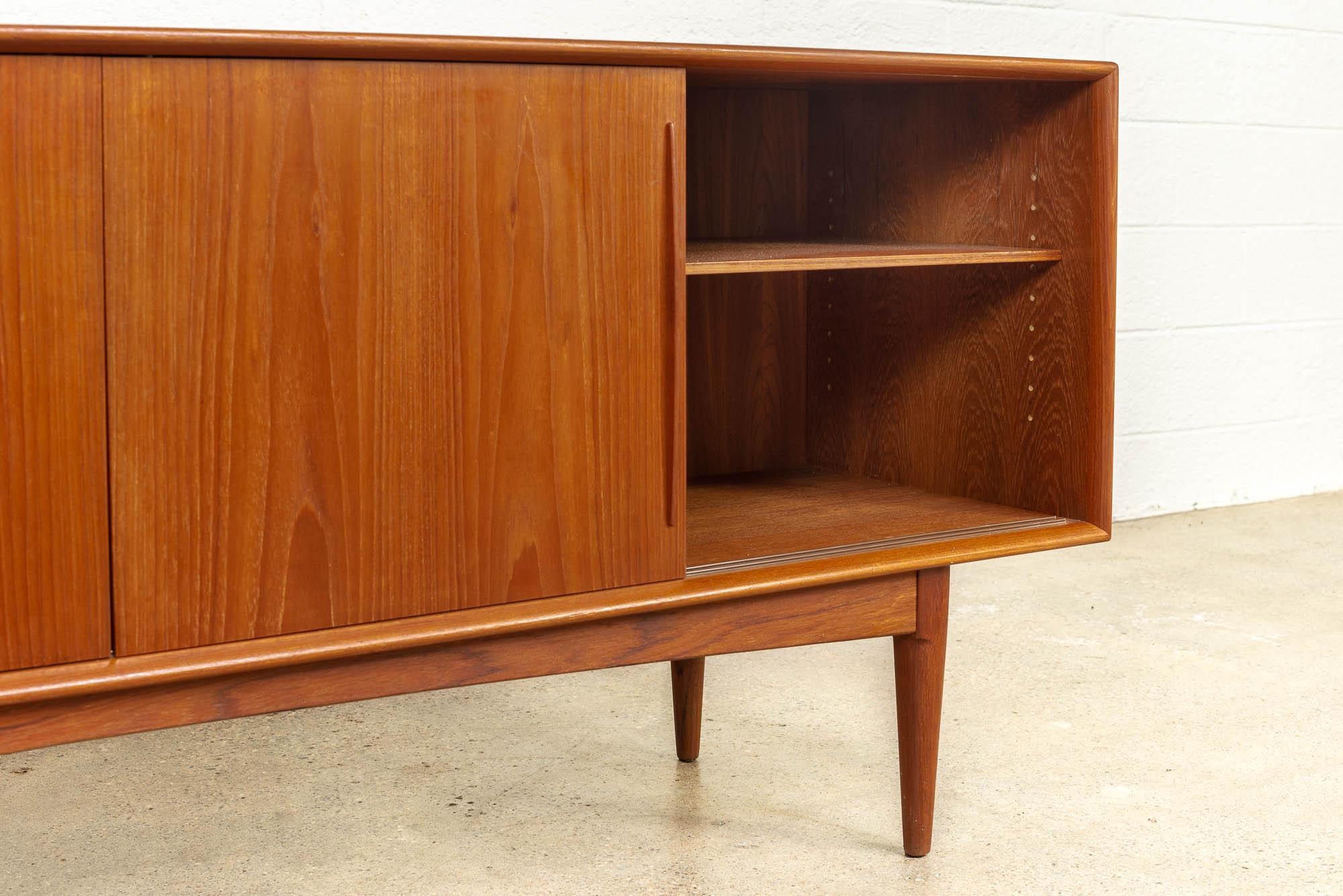 This exceptional vintage midcentury Danish modern Bernhard Pedersen & Son credenza sideboard was made in Denmark circa 1960. Expertly crafted from teak with beautiful grain pattern, this extra wide cabinet feature four sliding doors with sculpted