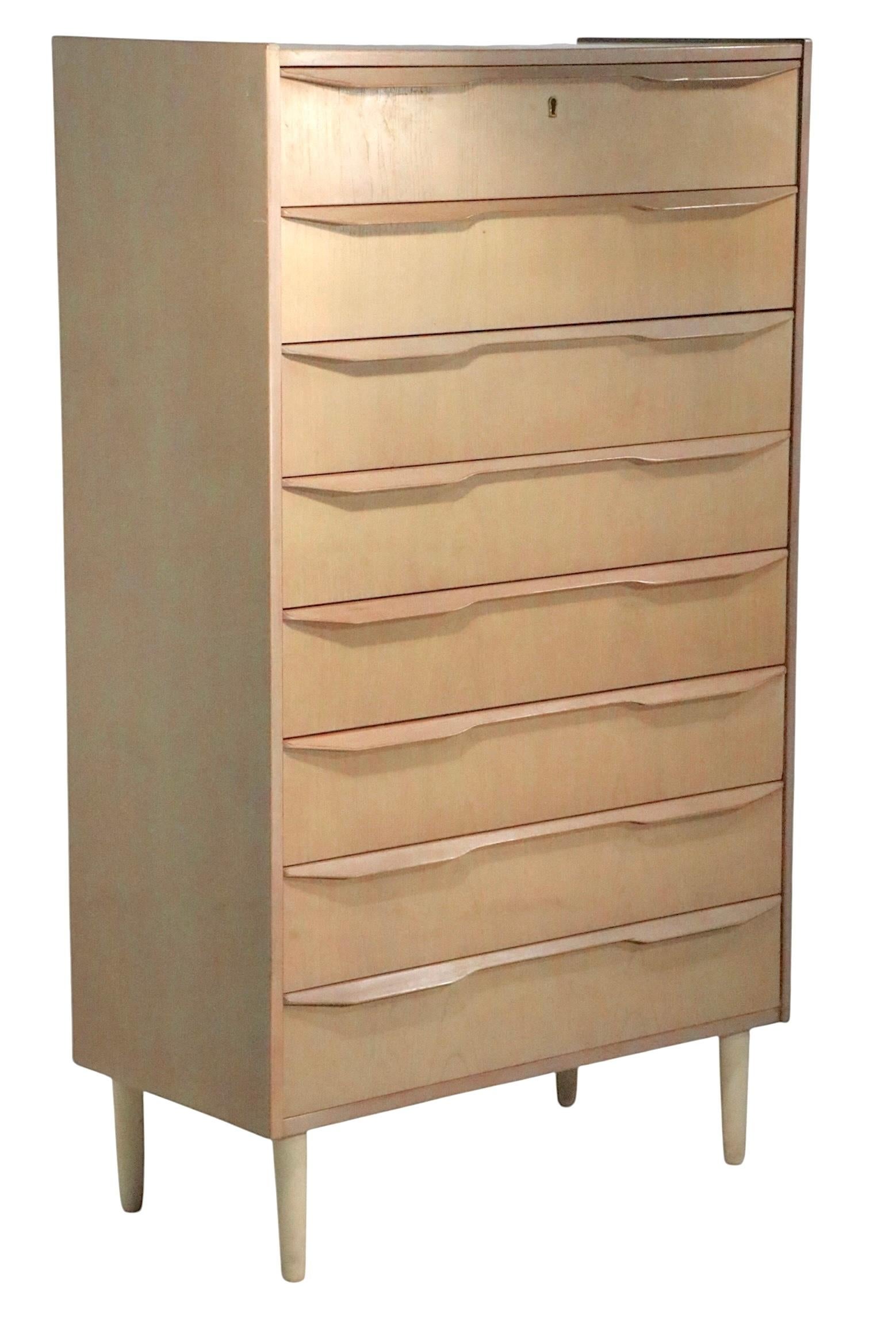  Cassettiera alta danese della metà del secolo scorso in stile insolito  con finitura chiara, ha otto cassetti, ciascuno con due tiretti in legno scolpito. Il comò poggia su quattro gambe affusolate in legno massiccio. Questo esemplare è in ottime