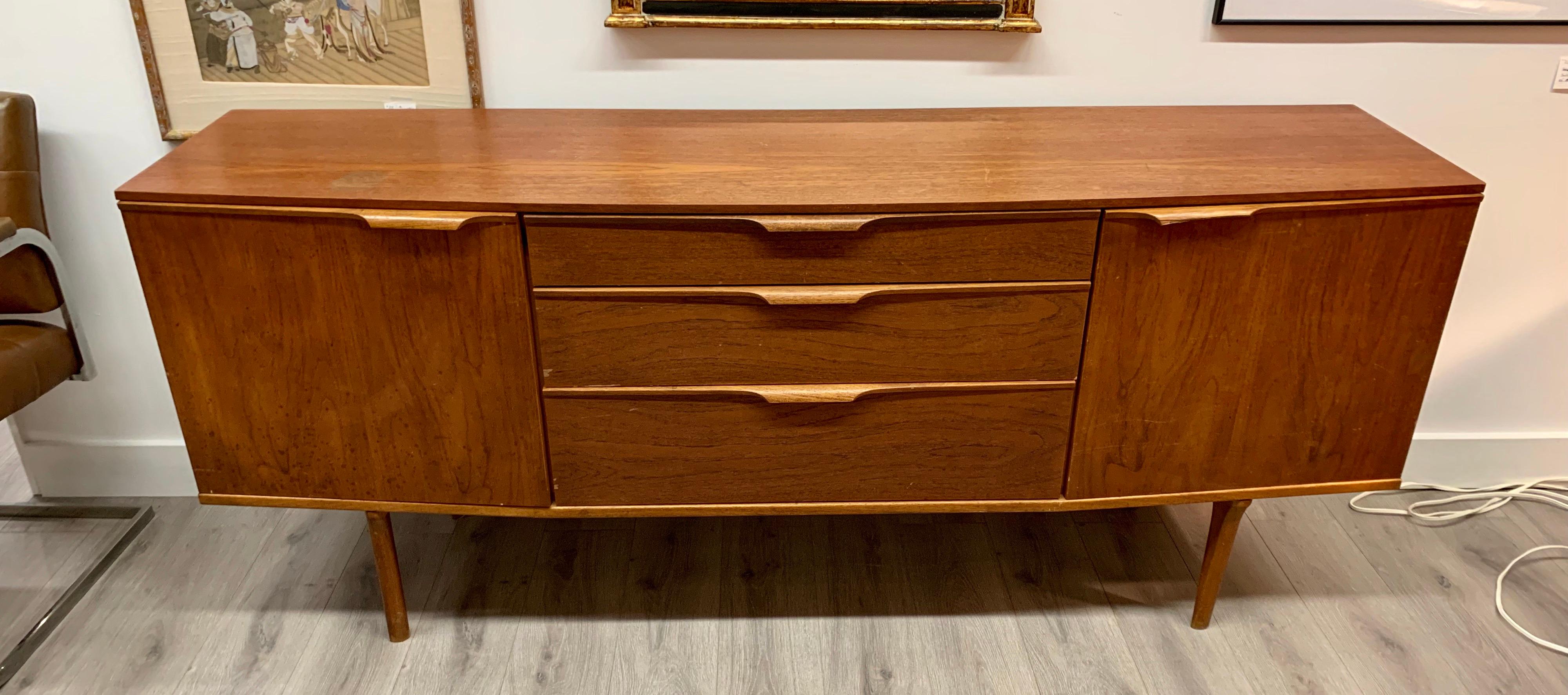 Unusual Danish modern bow front teak sideboard or server. The condition is fair and there is some
wear on the top as detailed in the pictures. There are three drawers in front as well as two compartments. Unsigned, circa 1960s.