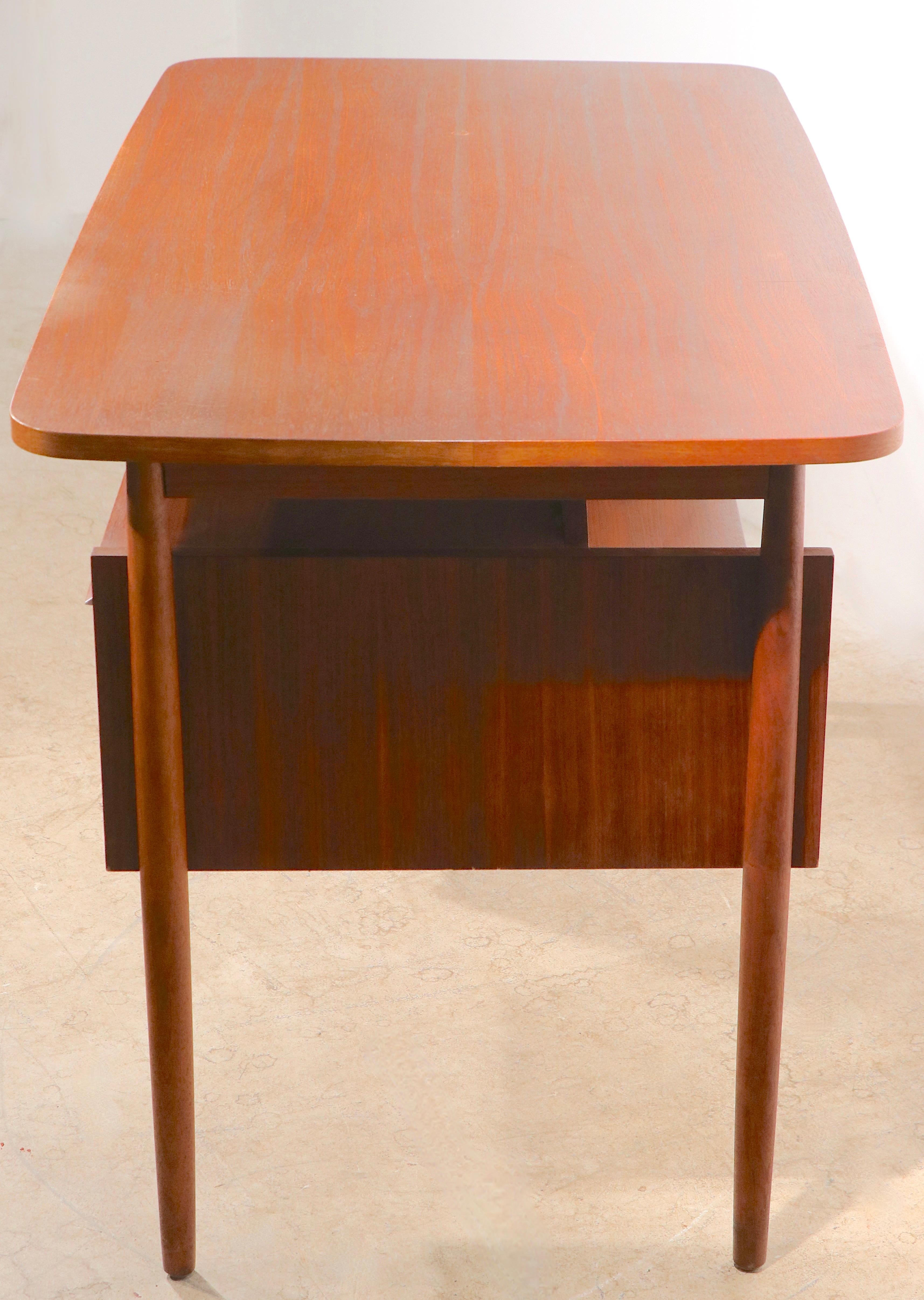 Classic Danish Mid Century Modern writing desk, designed by Gunnar Nielsen Tibergaard, executed in teak. The piece features two banks of two drawers and a bookcase style front section.  The desk is structurally  sound and sturdy, and fully