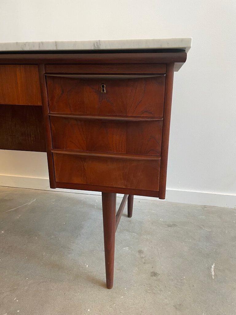 Mid-century Danish modern desk with added marble top. This teak desk with brass detailing comes with a working lock and key and seven storage drawers.