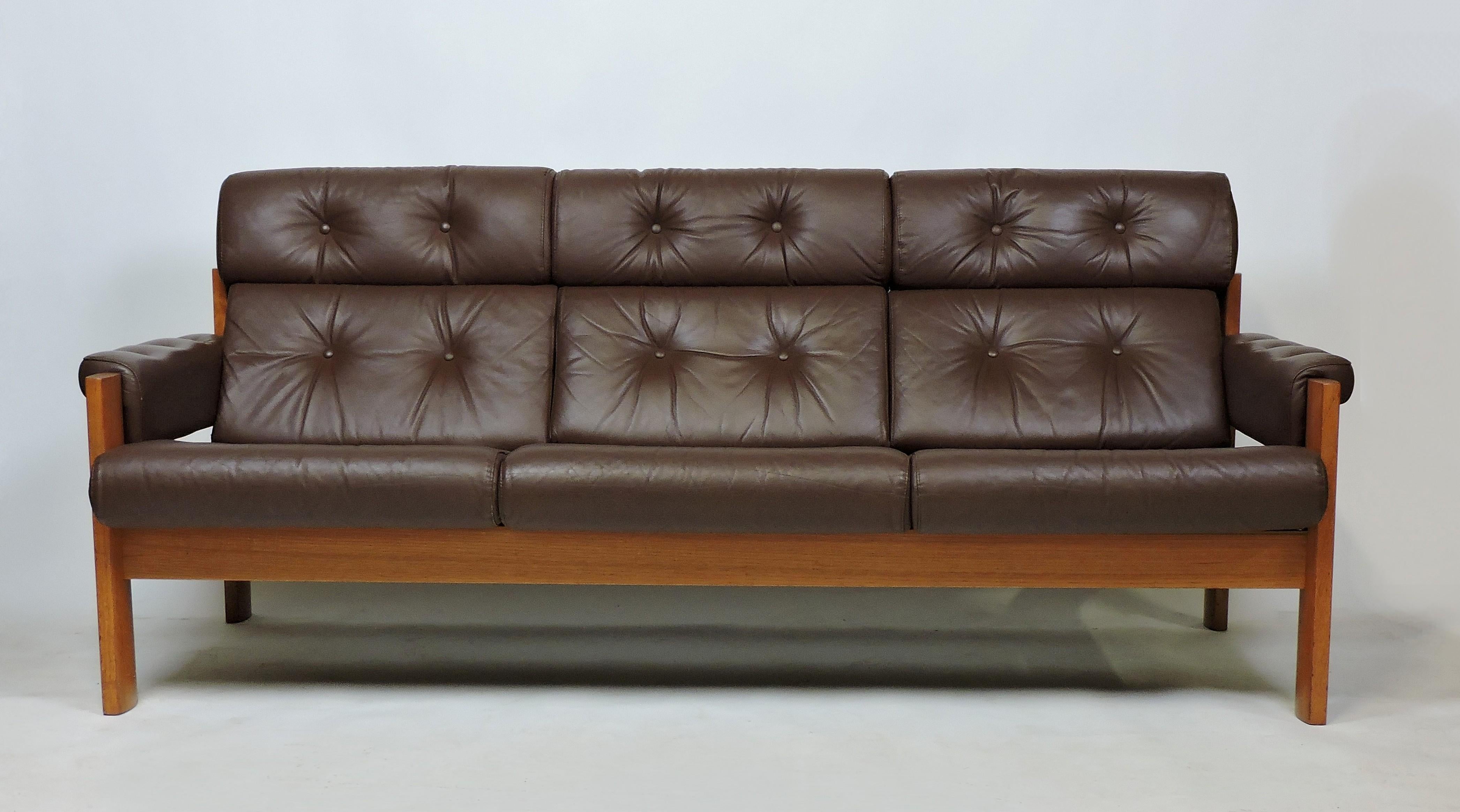 Handsome and comfortable three-seat Amigo sofa made in Norway by high quality furniture manufacturer, Ekornes. It has great craftsmanship with a sculpted solid teak frame and dark brown tufted leather and fabric upholstery. All of the cushions are