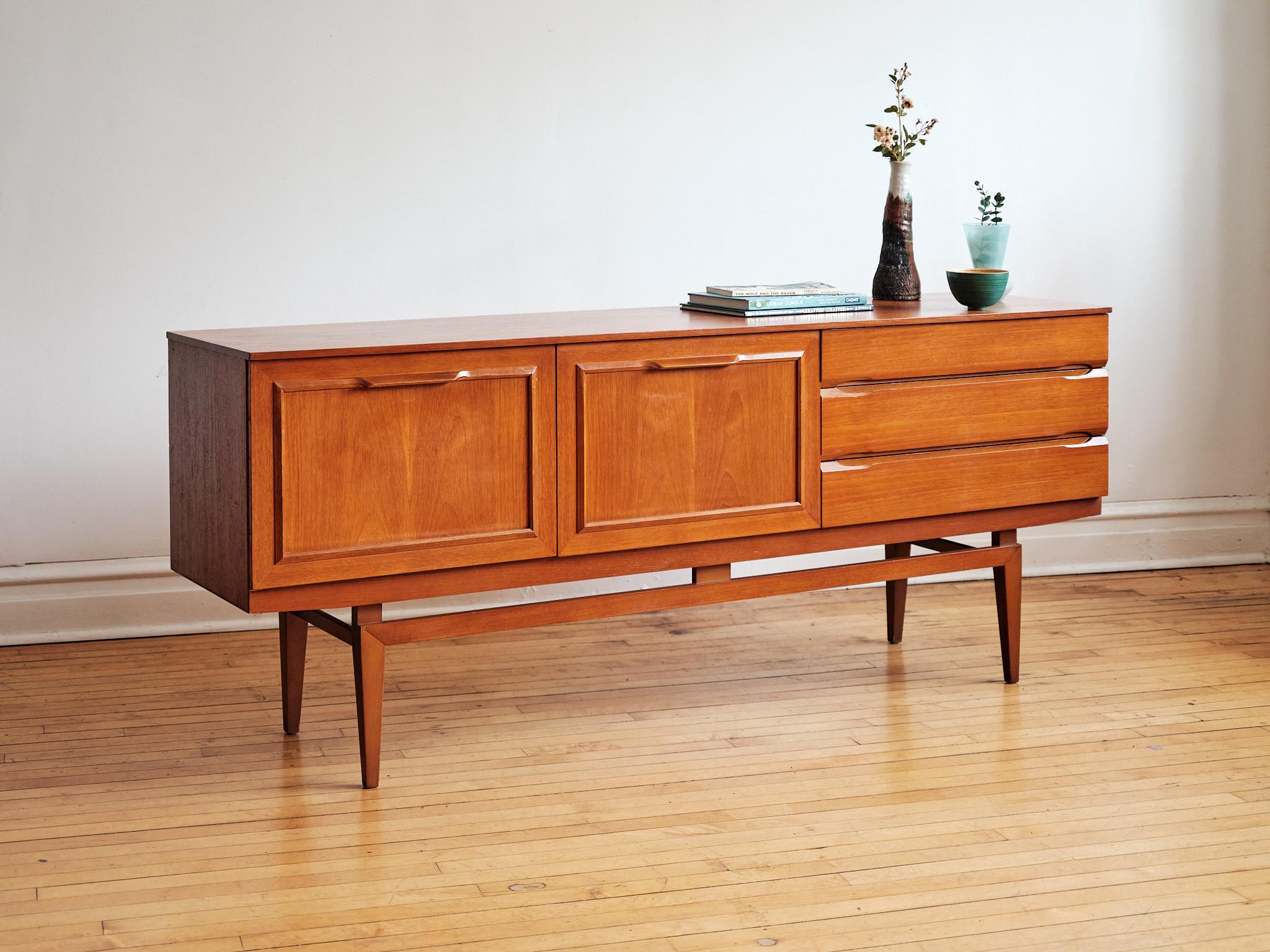 Mid-century Danish Modern floating teakwood sideboard.
Just imported from England to Chicago. 
Unknown designer.
This piece includes three drawers; the top drawer holds dividers.
Two cabinets hold shelving inside; the center cabinet is a drop