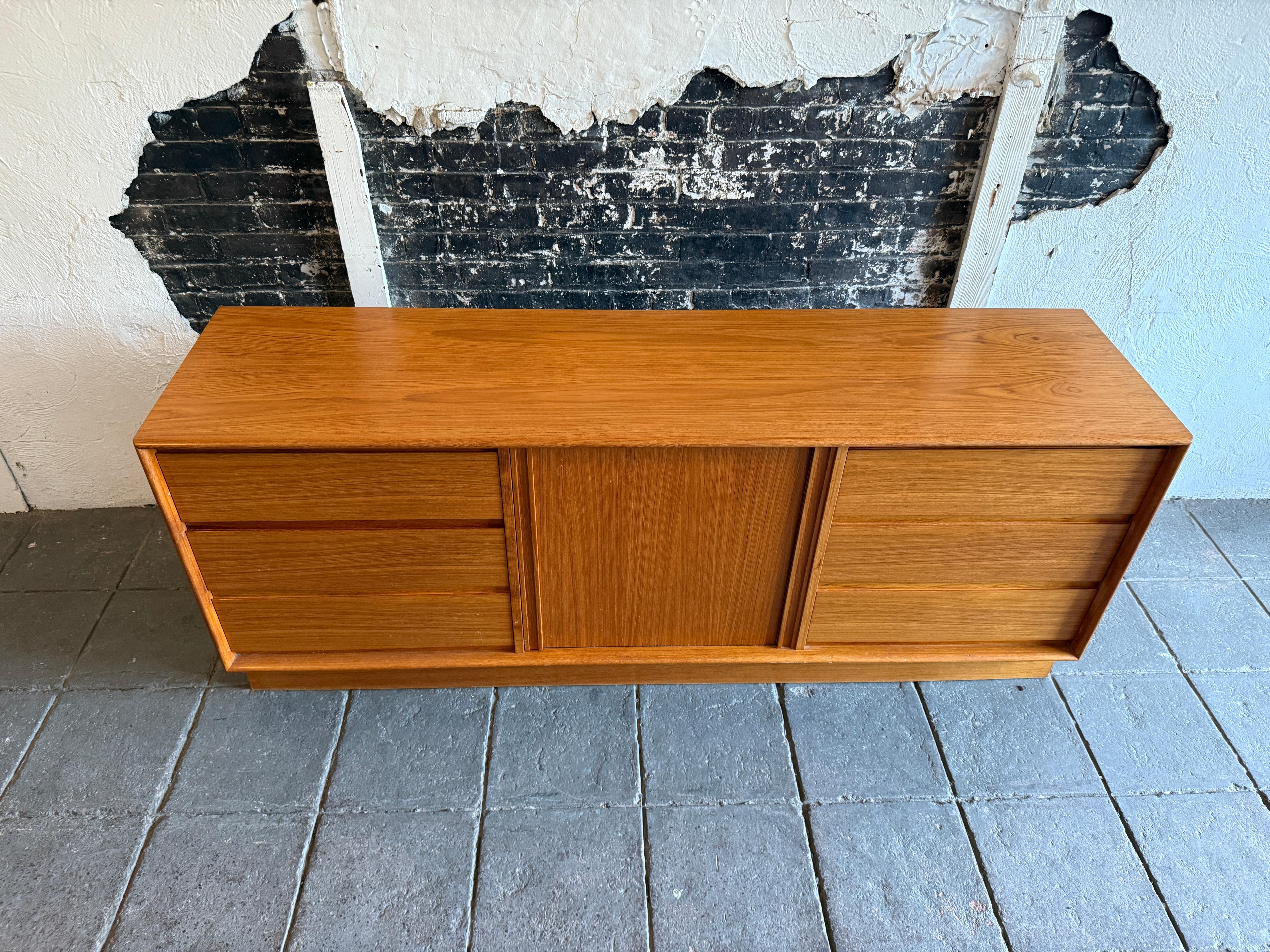 Very Clean Mid century danish modern long light teak dresser by Art furn. Simple basic Danish modern design teak 6 drawer dresser. Has carved upper and lower handles with solid wood drawers with nice dovetail joints. Has center tambour sliding door