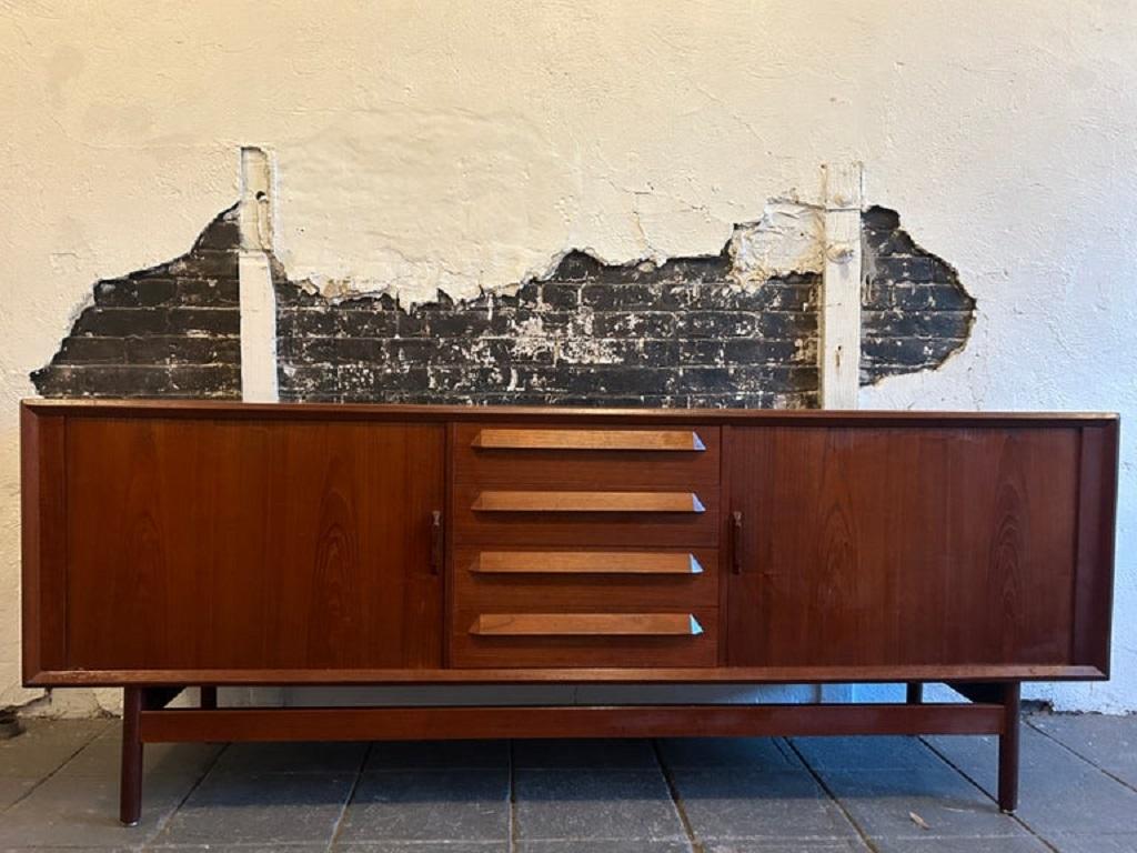 Splendida credenza in teak moderna danese di metà secolo con (2) ante a tamburo di Kofod Larsen. Una bella coppia di ante a tamburo rivela (3) ripiani regolabili e (1) cassetto rivestito in feltro. Ha (4) cassetti centrali in teak con gambe e