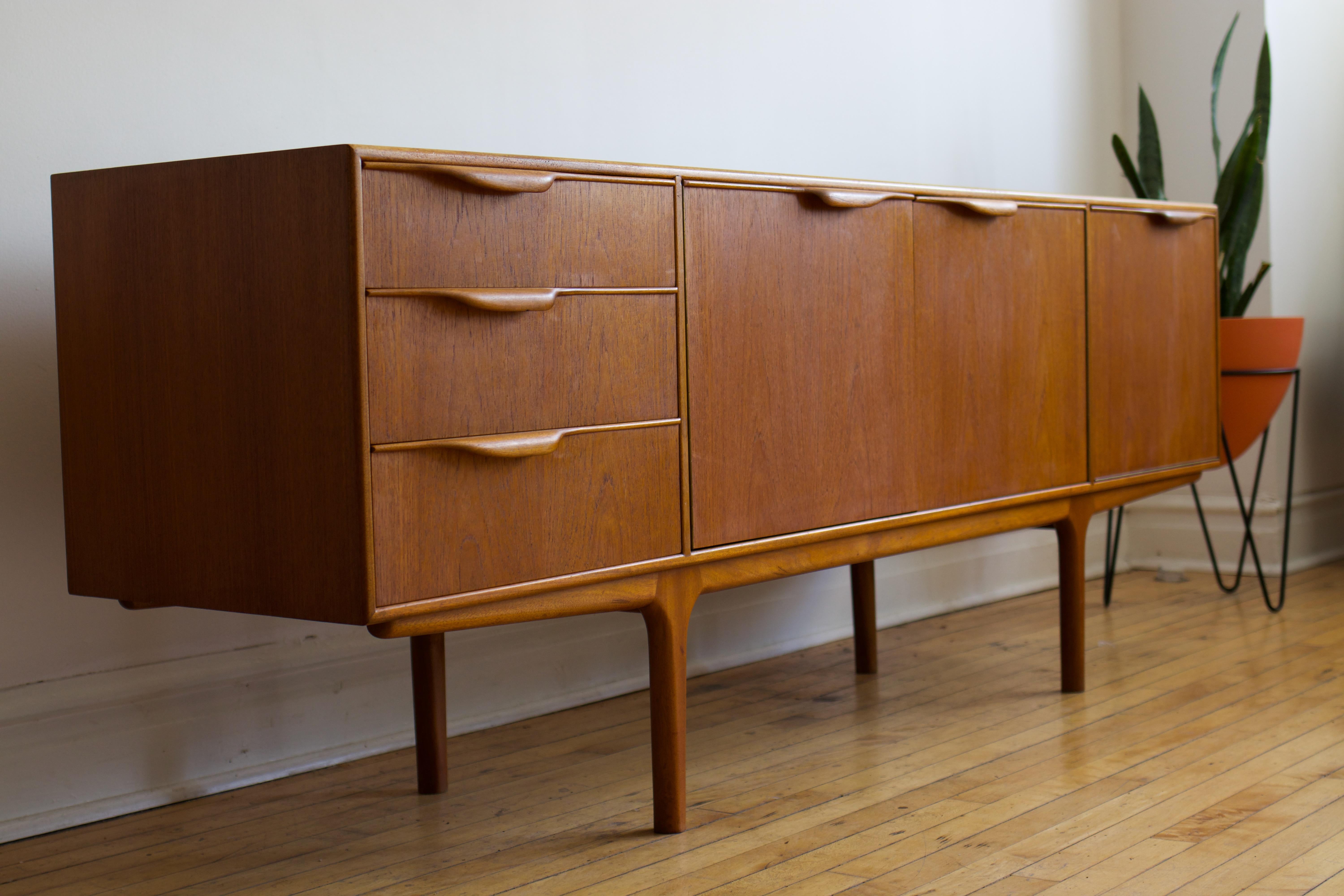 Mid-Century Modern teak wood bar cabinet.
Just imported from England to Chicago. Made in Scotland by McIntosh.
Delicately curled wooden handles.
Features a unique base with leg inlays. 
Three dovetailed drawers; top drawer holds built-in