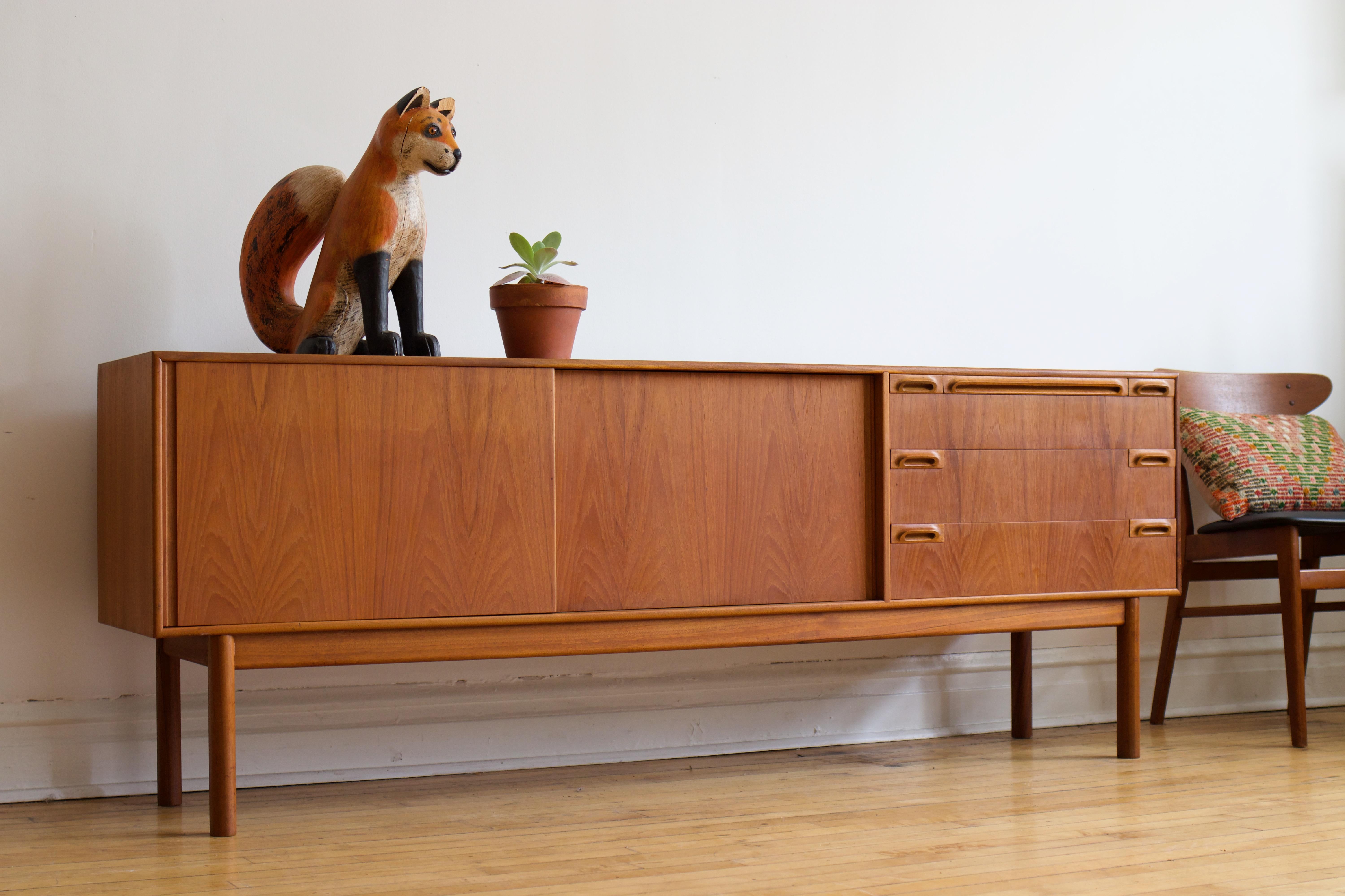 Extra long Mid-century Modern teakwood sideboard.
Made in Scotland by McIntosh.
Just imported from England to Chicago.
Gorgeous teak wood grain and uniquely carved pulls.
Three drawers; top drawer holds dividers.
Black laminated tray extends for