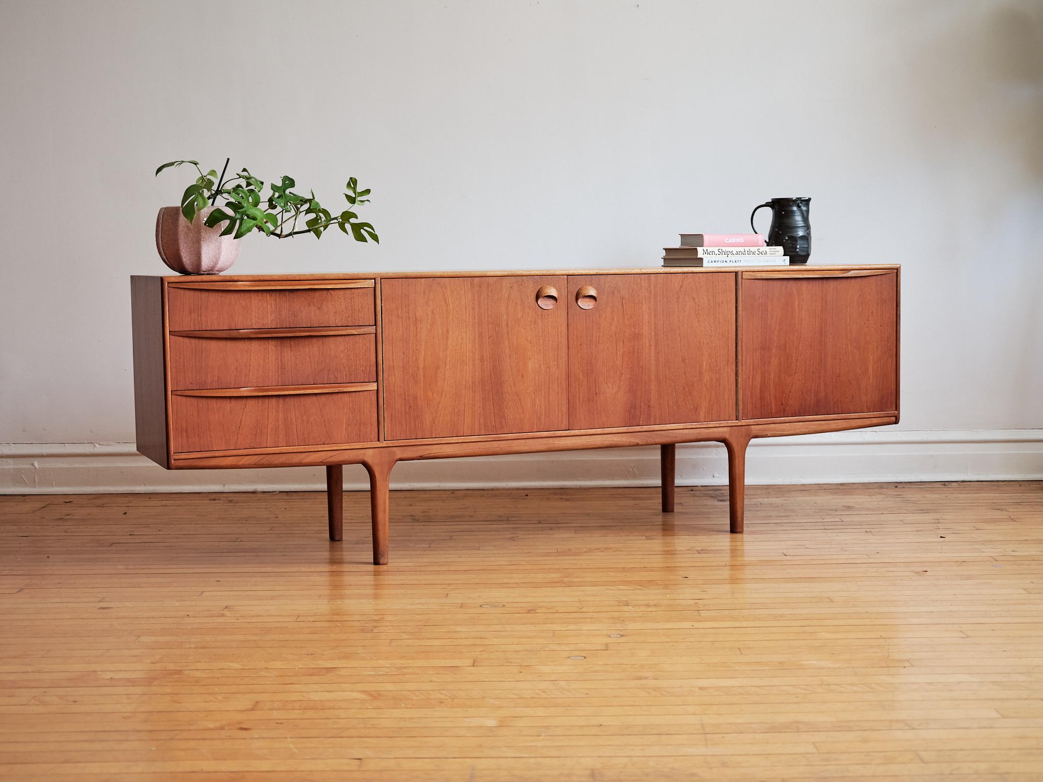 Mid-Century Modern teak wood credenza.
Just imported from England to Chicago. 
Made in Scotland by McIntosh.
Beautifully carved wooden handles.
Features a unique base with leg inlays.
Three dovetailed drawers; top drawer holds built-in