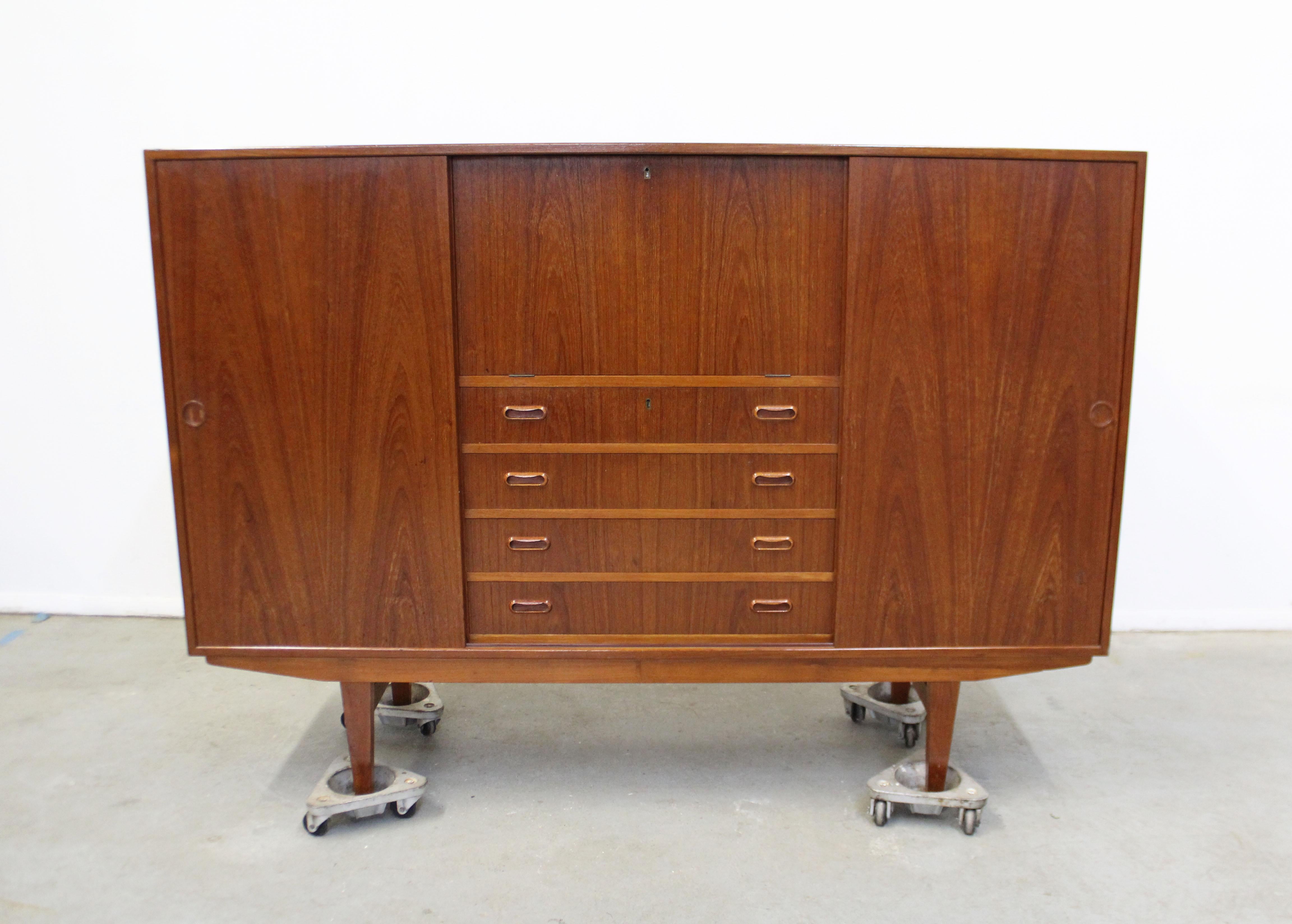 Offered is a teak credenza/highboard by Omann Jun. Features sliding doors with shelving, 4 drawers, and a pull-down surface. Comes with a key to lock drawers and secretary. It is in great condition, showing some age wear, (surface scratches/chips,