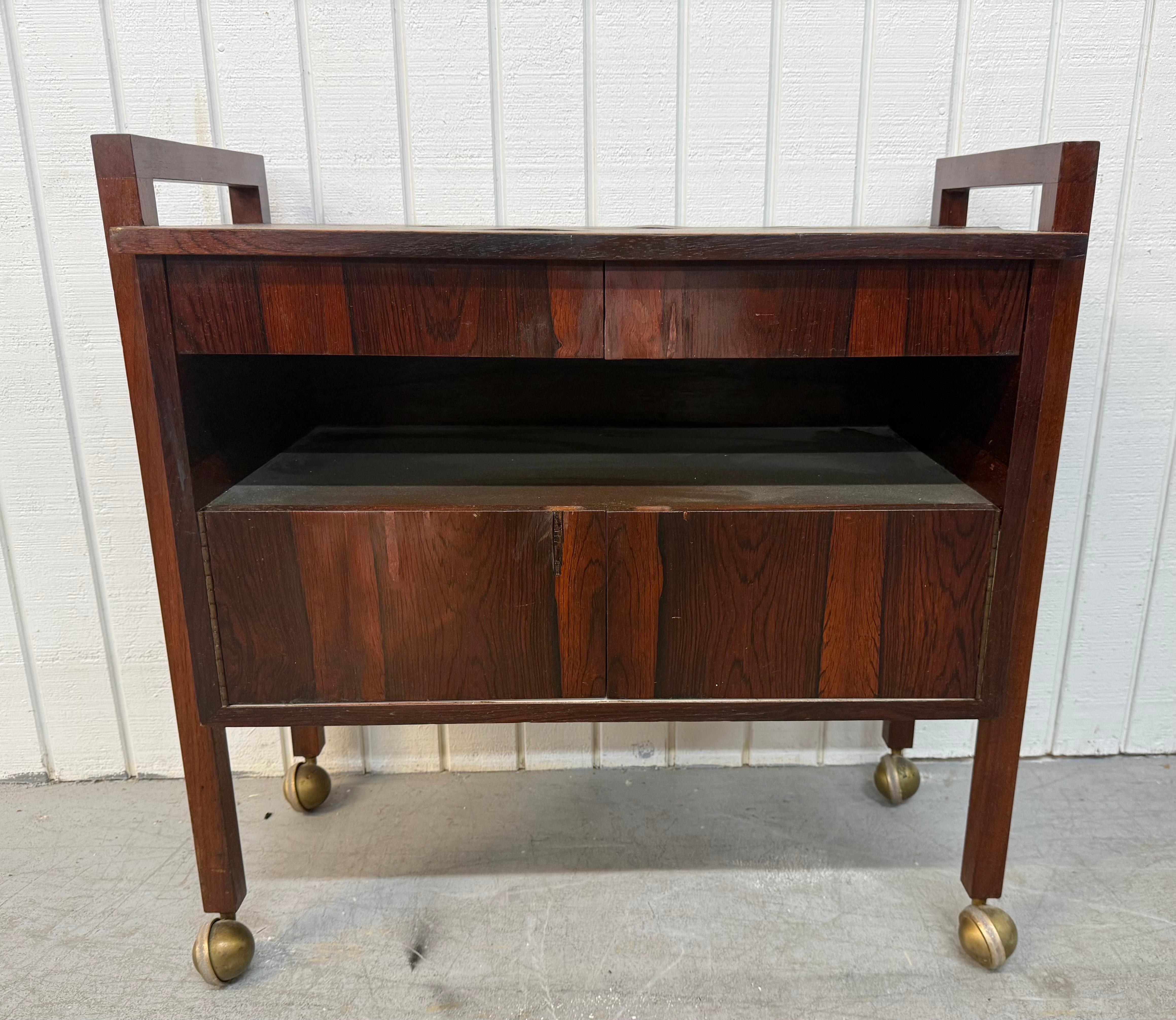 This listing is for a Mid-Century Danish Modern Rosewood Bar Cart. Featuring a straight line design, two drawers at the top, two doors at the bottom that open up to storage space, long modern legs on casters for easy movement, finished back side,