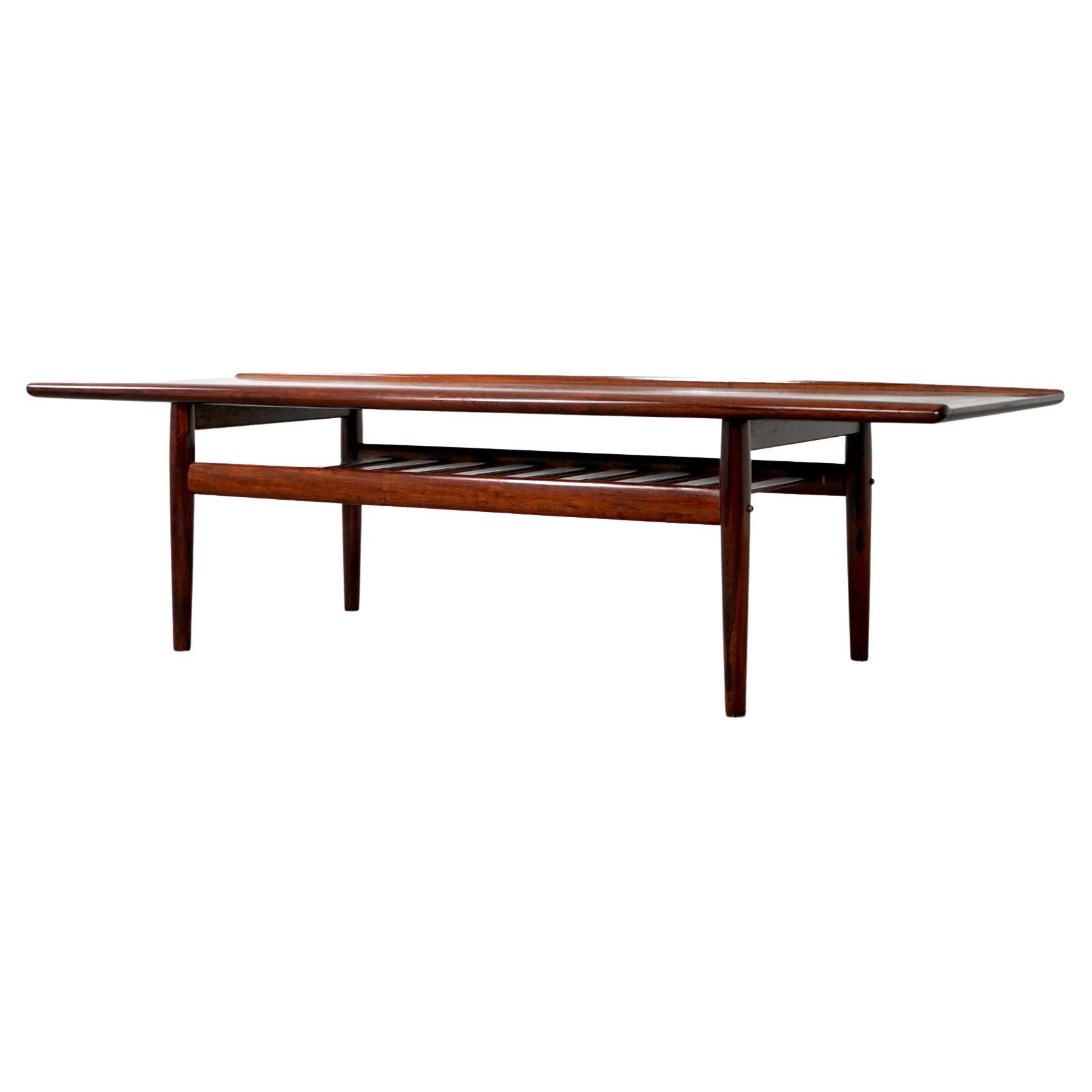 Rosewood Danish coffee table by Grete Jalk, circa 1960's. Top shows stunning book matched veneer and solid wood curved edge along its length. Slatted shelf gives an airy impression and is perfect for magazines, remote controls and other things that