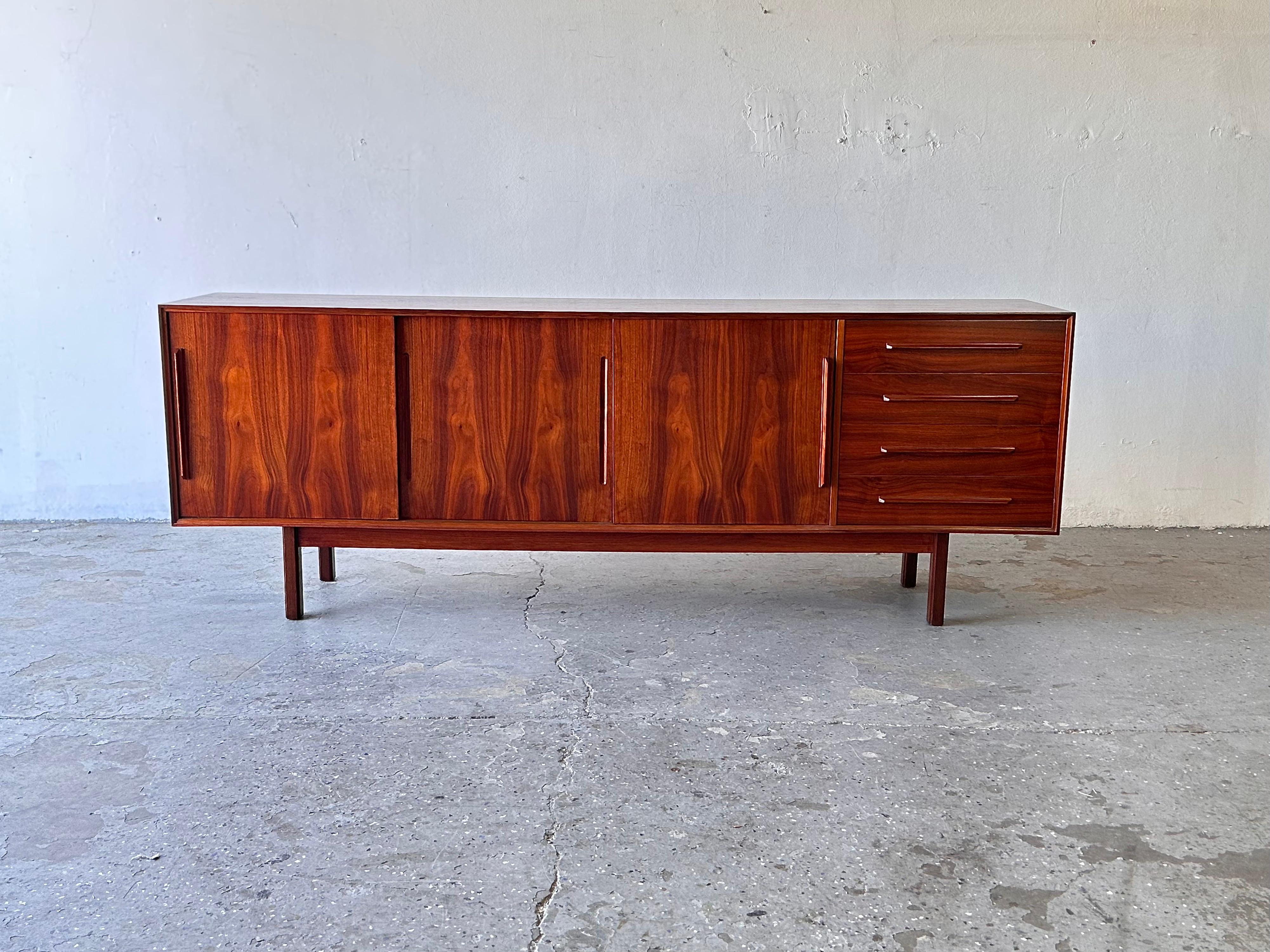 
Exceptional mid century Rosewood sliding door credenza or server by Ib-Kofod Larsen for Faarup Møbelfabrik made in Denmark, circa 1960’s. Beautifully rosewood  grained, extra long credenza. Features three sliding cabinet doors and four dovetailed