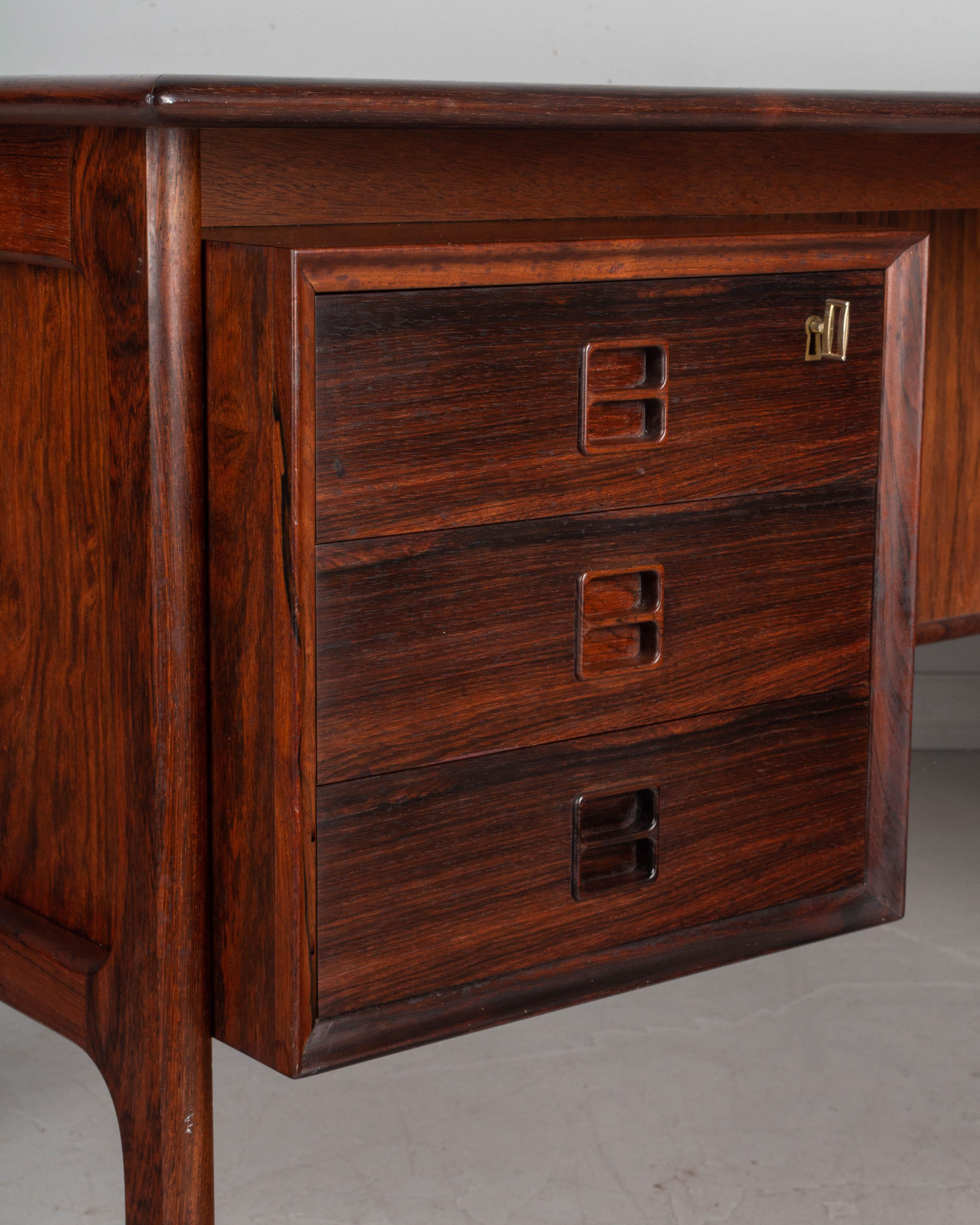A midcentury Danish modern rosewood executive desk by master craftsman, architect and designer Arne Vodder. Three dovetailed drawers with inset handles and working locks with two brass keys. Three bookshelf compartments on the back. Large work