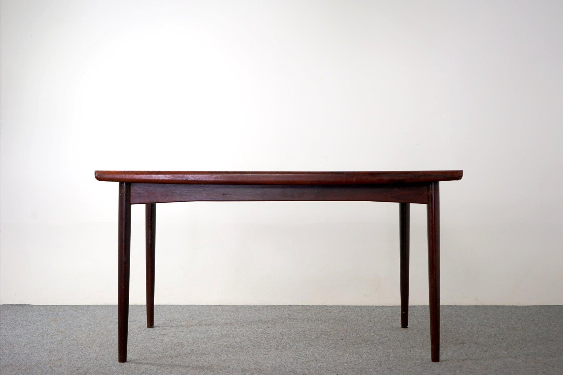 Rosewood Danish dining table, circa 1960's. Top is framed in solid wood edge trim while the center panels feature highly figured veneer with book-matched grain. Self-storing leaves slide out from each end to expand the table surface by nearly two