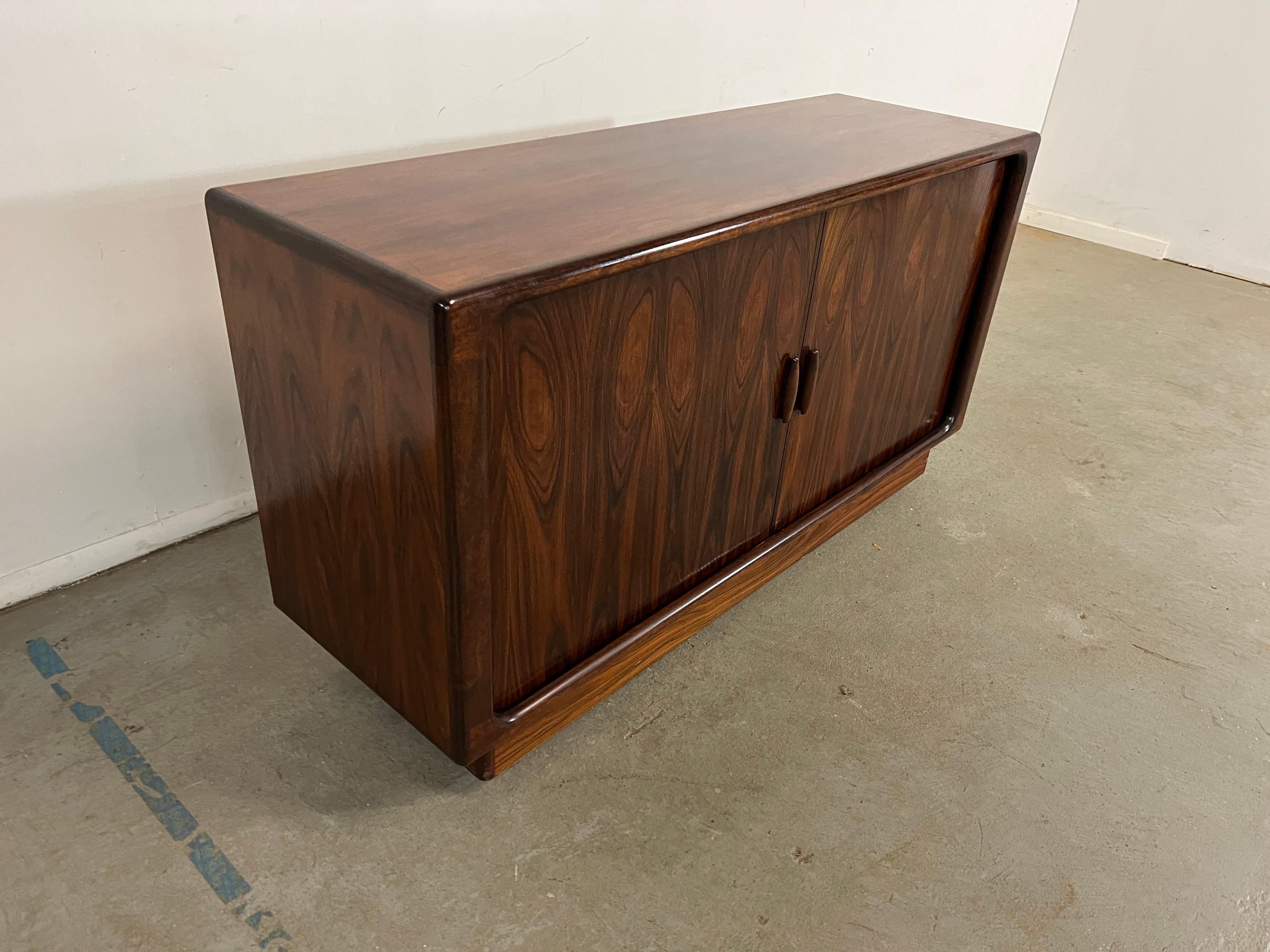 Mid-Century Danish Modern Rosewood Tambour Door Credenza
Offered is a rosewood credenza. It is made of rosewood, featuring two tambour doors on each side and  drawers inside.  It is in good condition, shows slight signs of wear (sun fade, surface ,