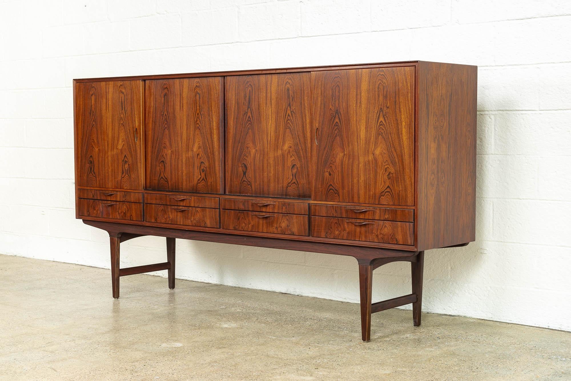 This striking midcentury Danish modern tall credenza or sideboard was made in Denmark, circa 1960. Exceptionally crafted, this rosewood cabinet features stunning grain pattern and all finished interiors, including the shelves and drawers. The upper