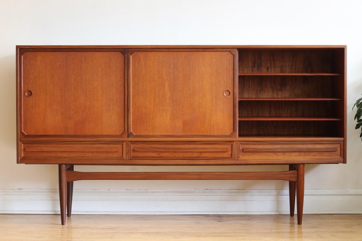 Mid-Century Modern Danish teak high credenza.
Just imported from Copenhagen.
Three sliding doors and three dovetailed drawers.
Features a long slender support bar.
All shelves are adjustable or removable.
Left cabinet holds green felt-lined