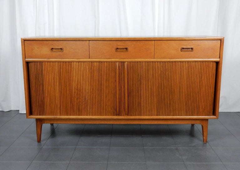 Handsome Danish blond sideboard with center
split tambour door cabinets and 3 drawers up top.
Inside cabinets each have a single adjustable shelf.
One top drawer has felt lined bottom with dividers.
It is in fine condition with smooth doors and