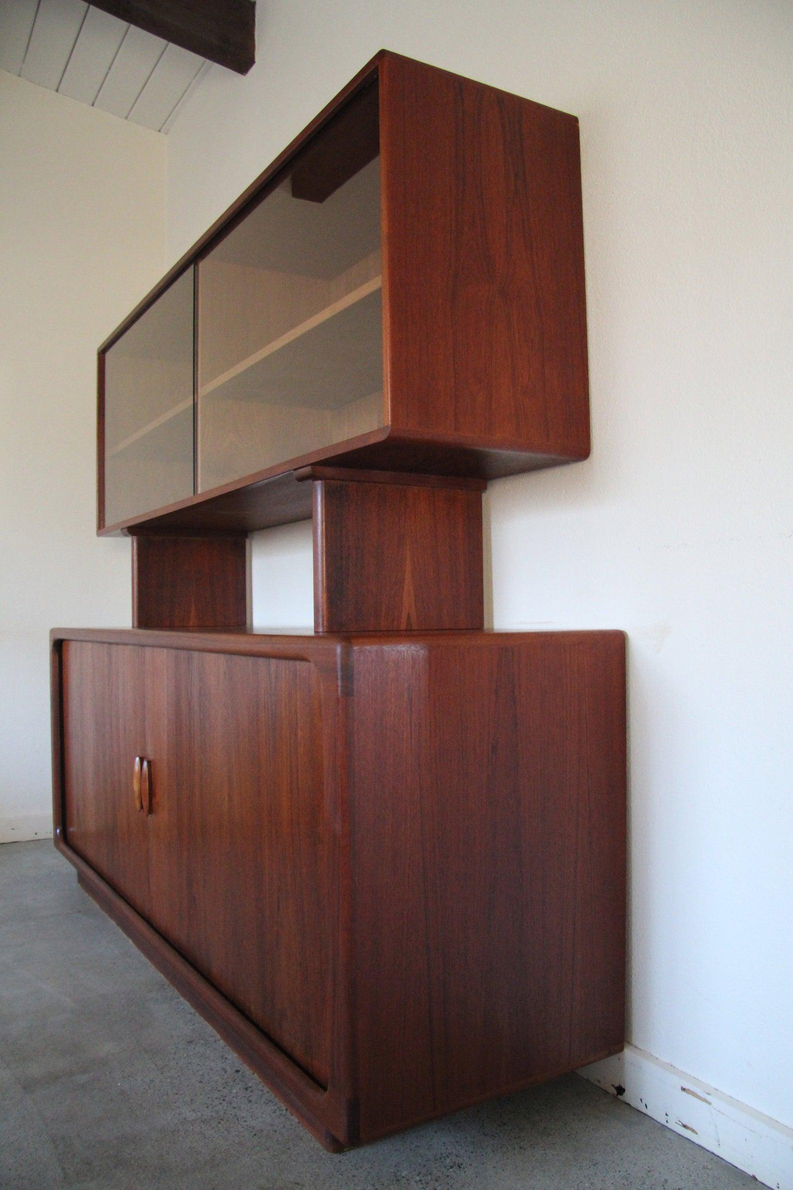 Danish modern teak credenza hutch has a removable top piece that has sliding glass doors that open to shelving. Bottom piece has two tambour doors with carved teak handles that open to adjustable shelves.