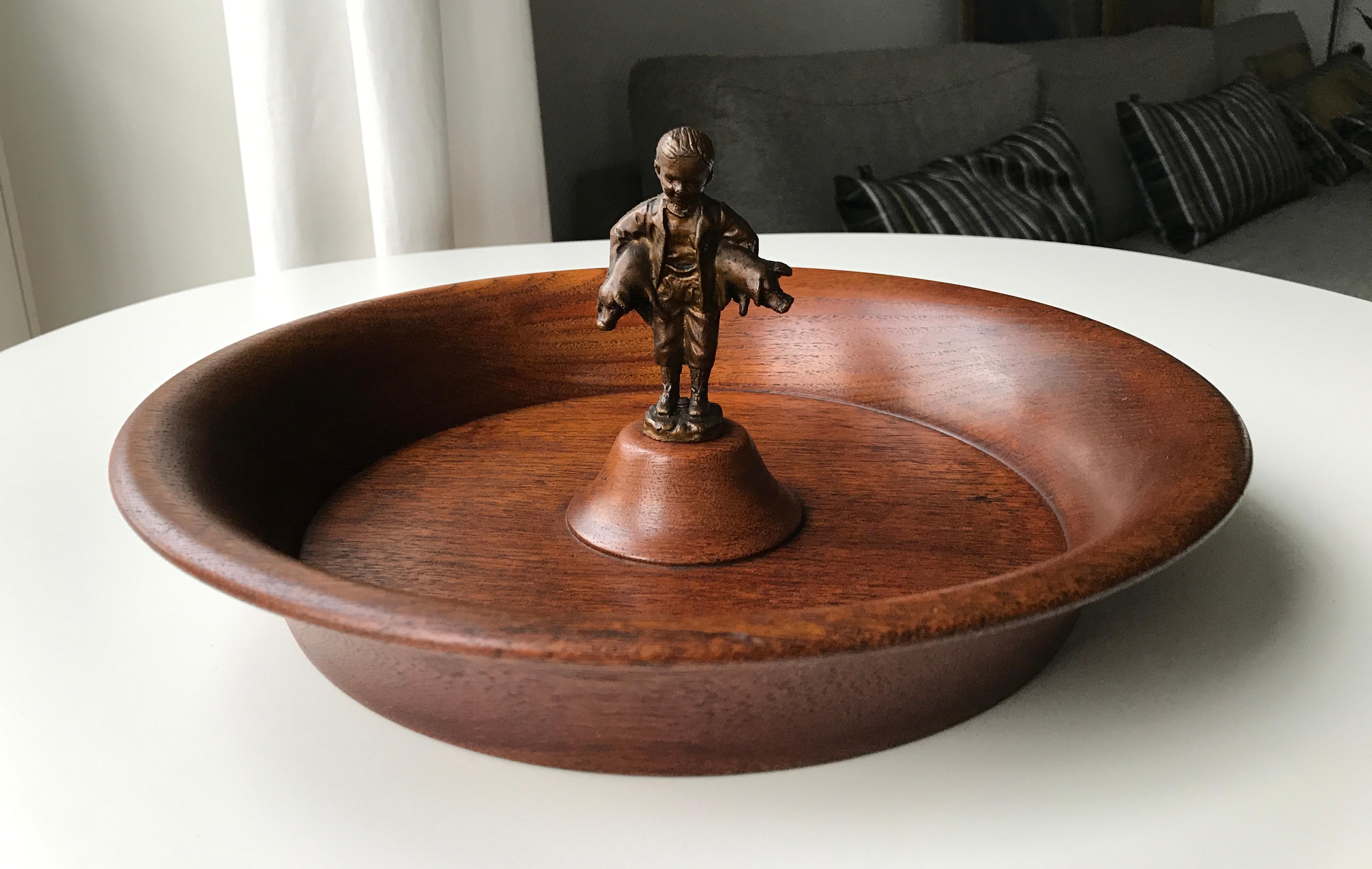 Mid-Century Mid-Century Modern design circular teak bowl with figurine of little boy holding two small piglets in his arms in metal presumably brass or bronze. Very lively in expression. The bowl is in solid teak wood in very good condition. No