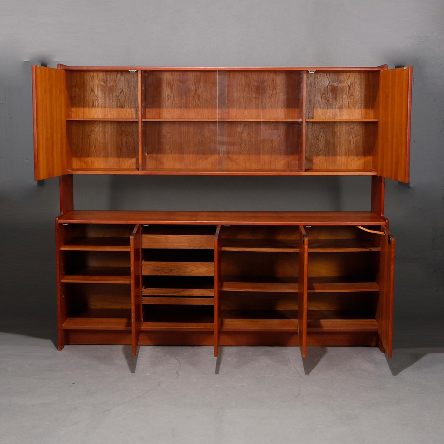 A midcentury Danish Modern sideboard offers teak construction with upper case having sliding glass doors cabinets flanked by blind doors surmounting lower with four blind door cabinets opening to interiors with shelves and sliding drawers, 20th