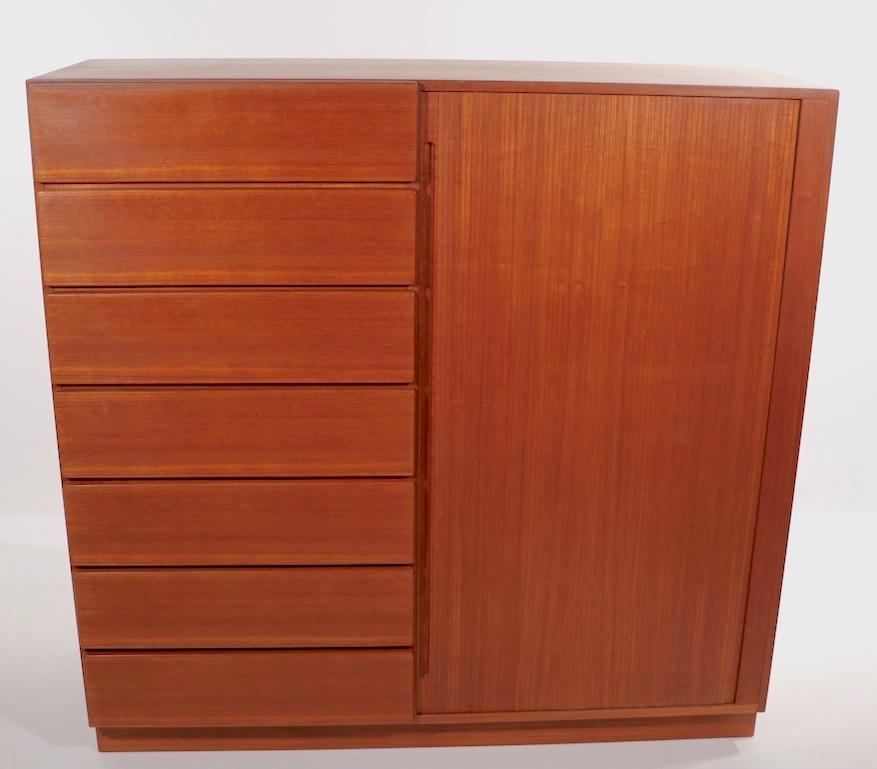Stylish architectural Danish modern wardrobe in teak, having a tambour door which opens to (5) interior drawers, flanked by (7) exterior drawers. This example is in extra clean, original and ready to use condition. Marked Made in Denmark in stencil