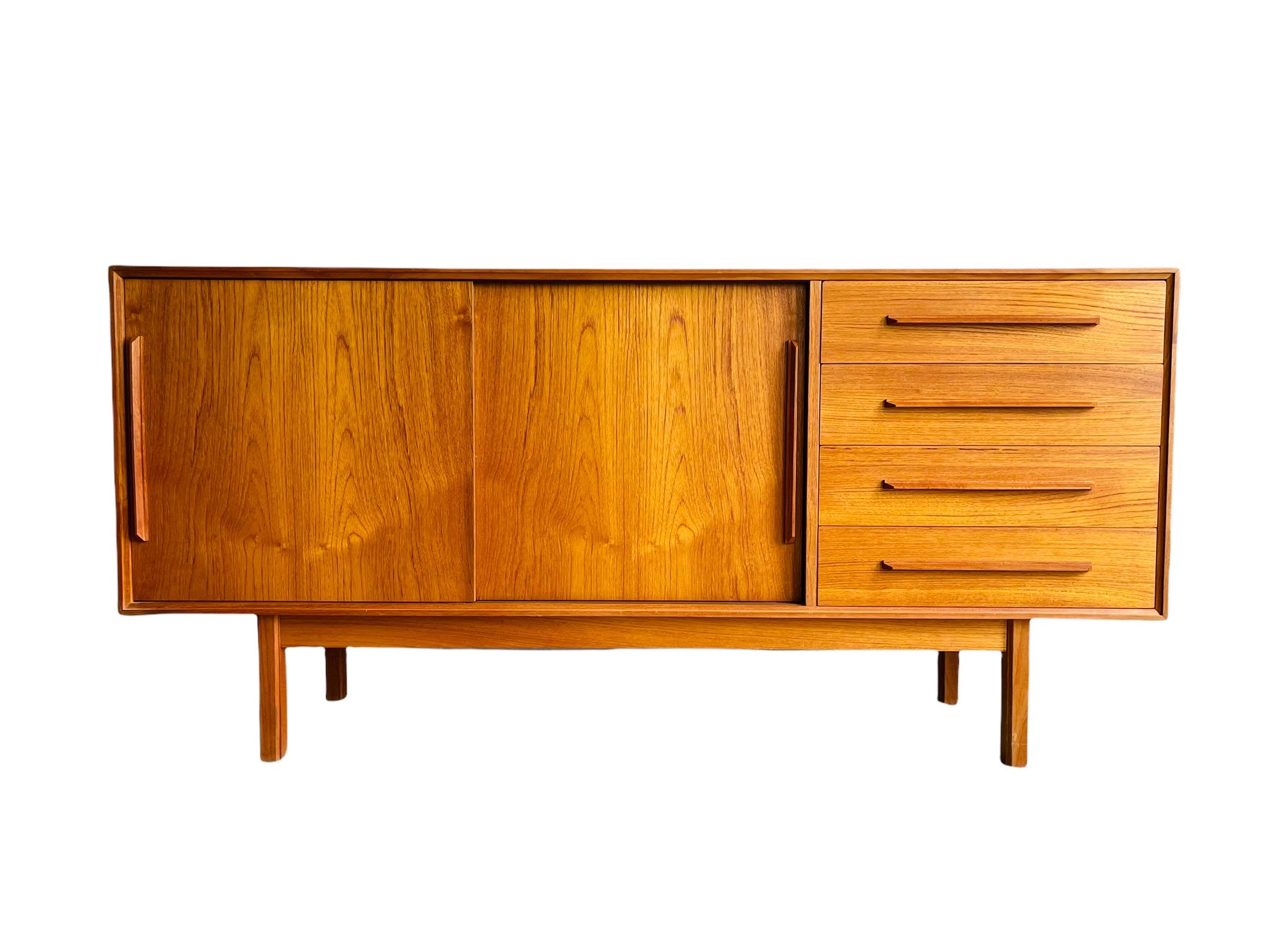 Mid-Century Modern Teak Credenza with four drawers, two sliding doors that open to plenty of storage space. This credenza is in good vintage condition with normal wear consistent with age and use. 

Measures: W 60.5” x D 17.5” x H 29”.
